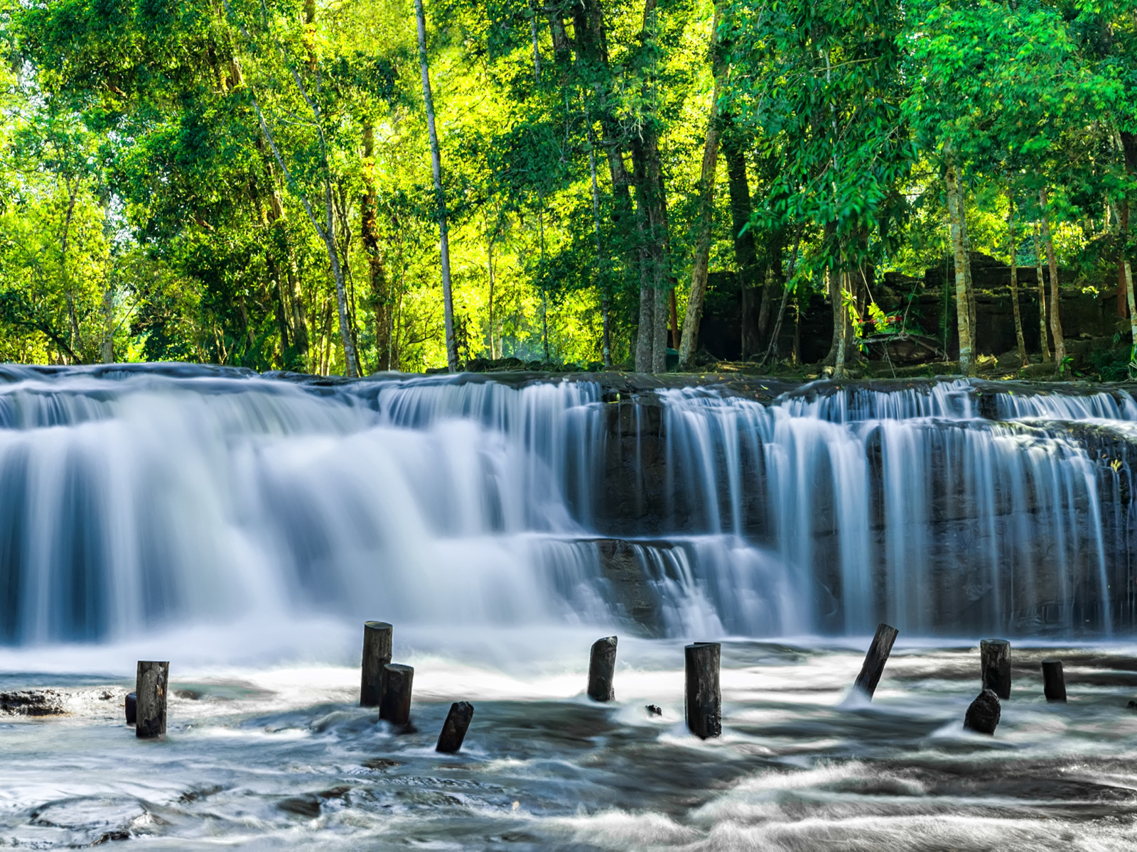 Водопад стекает с камней у зеленых деревьев