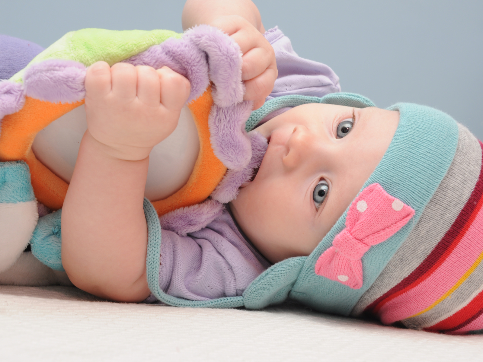 Младенец в шапке грызет мягкую игрушку