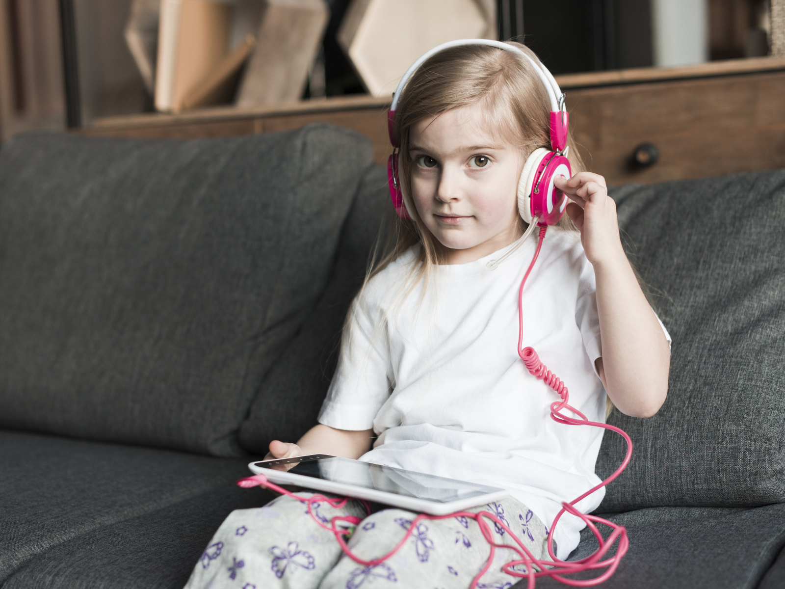 Девочка сидит на диване в наушниках  и с планшетом