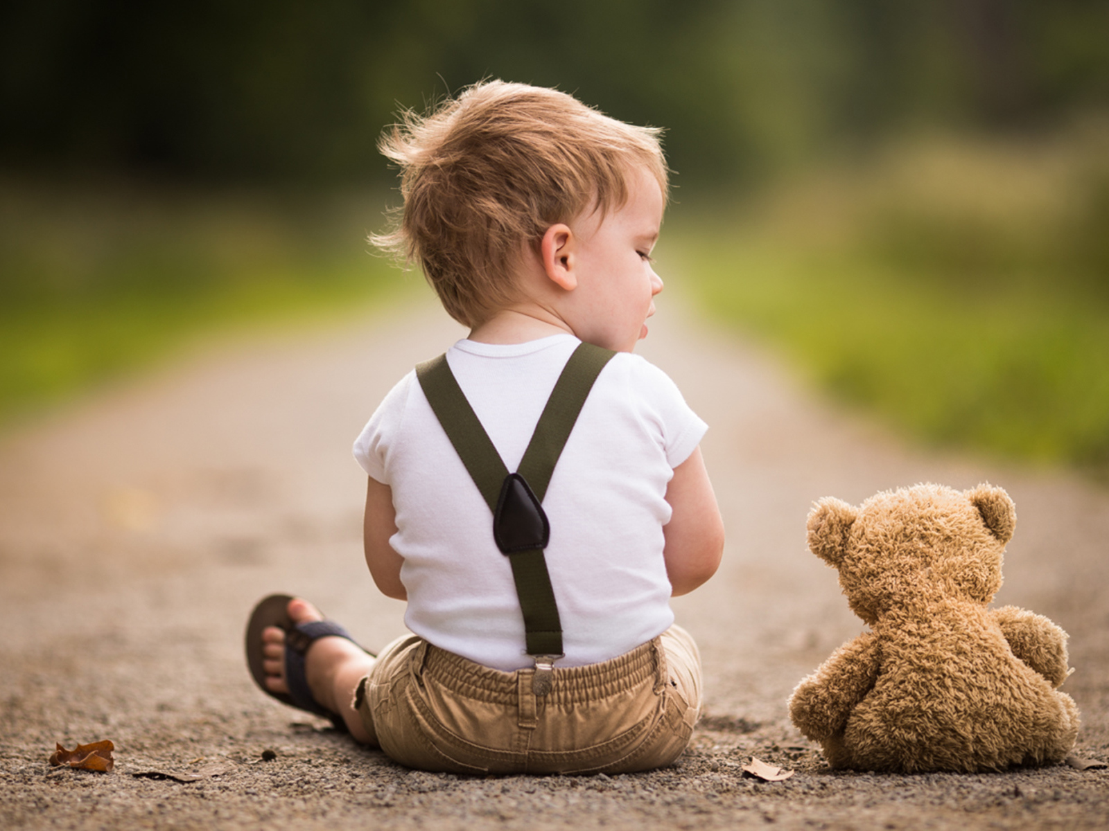 Маленький мальчик сидит на дороге с игрушечным мишкой