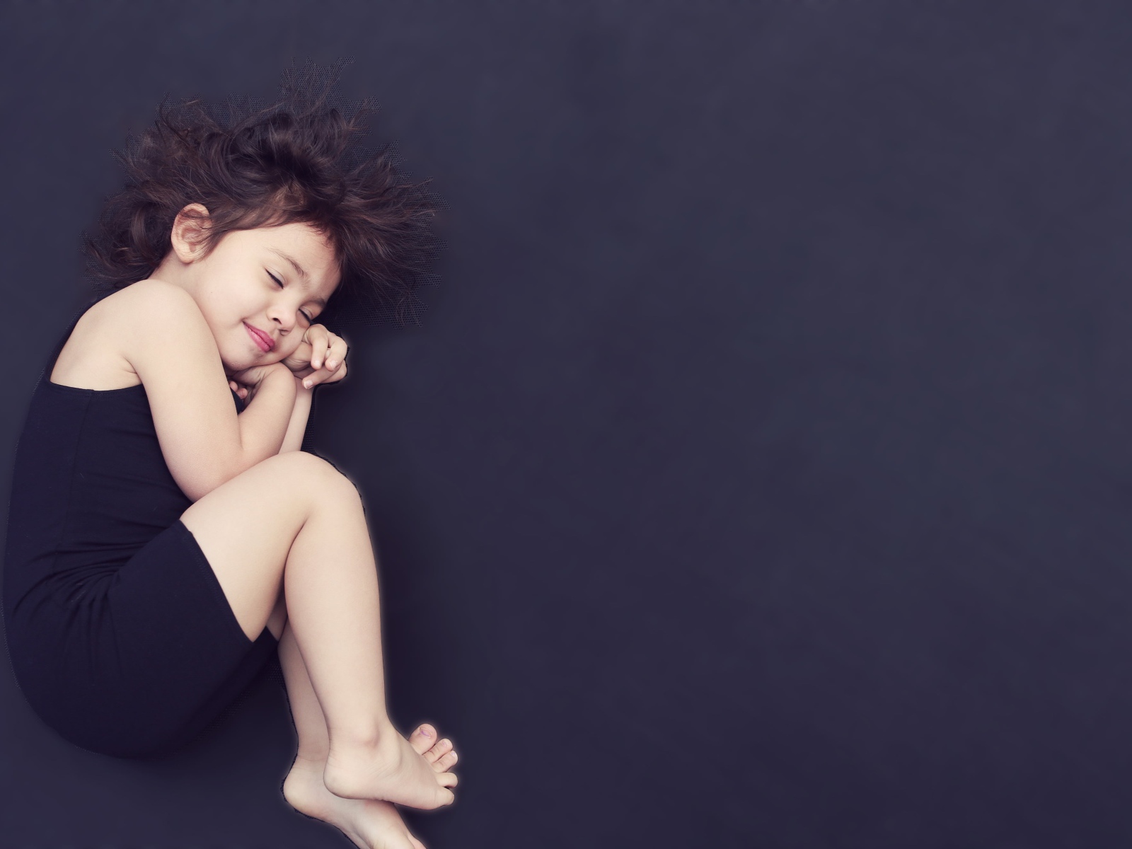 Маленькая девочка в черном платье спит на черном фоне