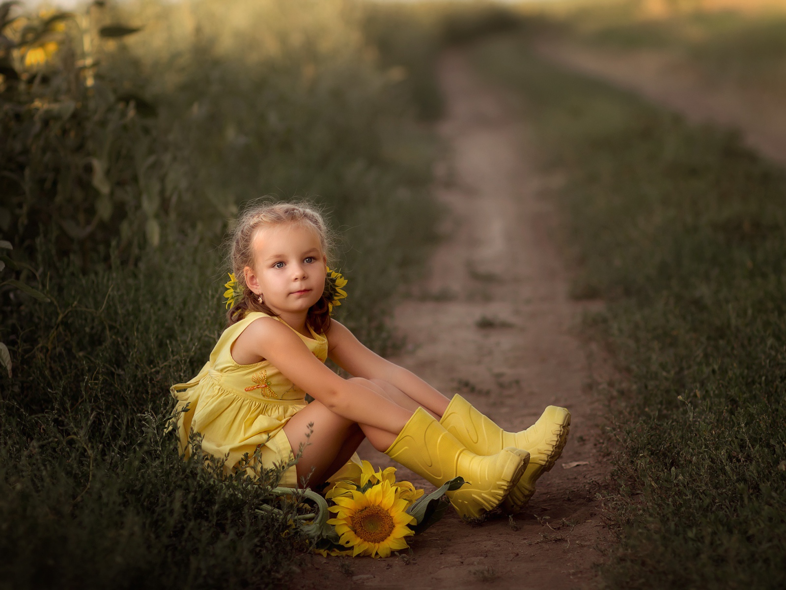 Маленькая девочка в желтом платье сидит на земле с подсолнухами