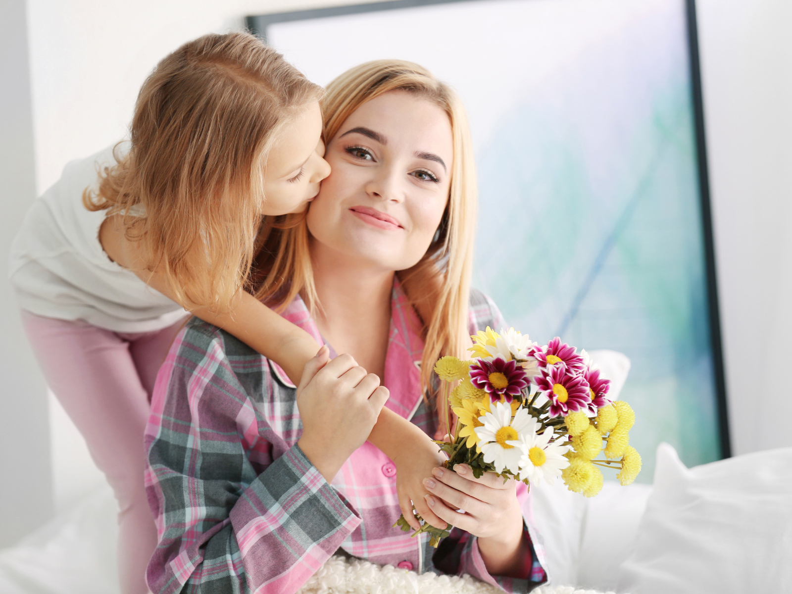 Маленькая девочка целует маму с букетом