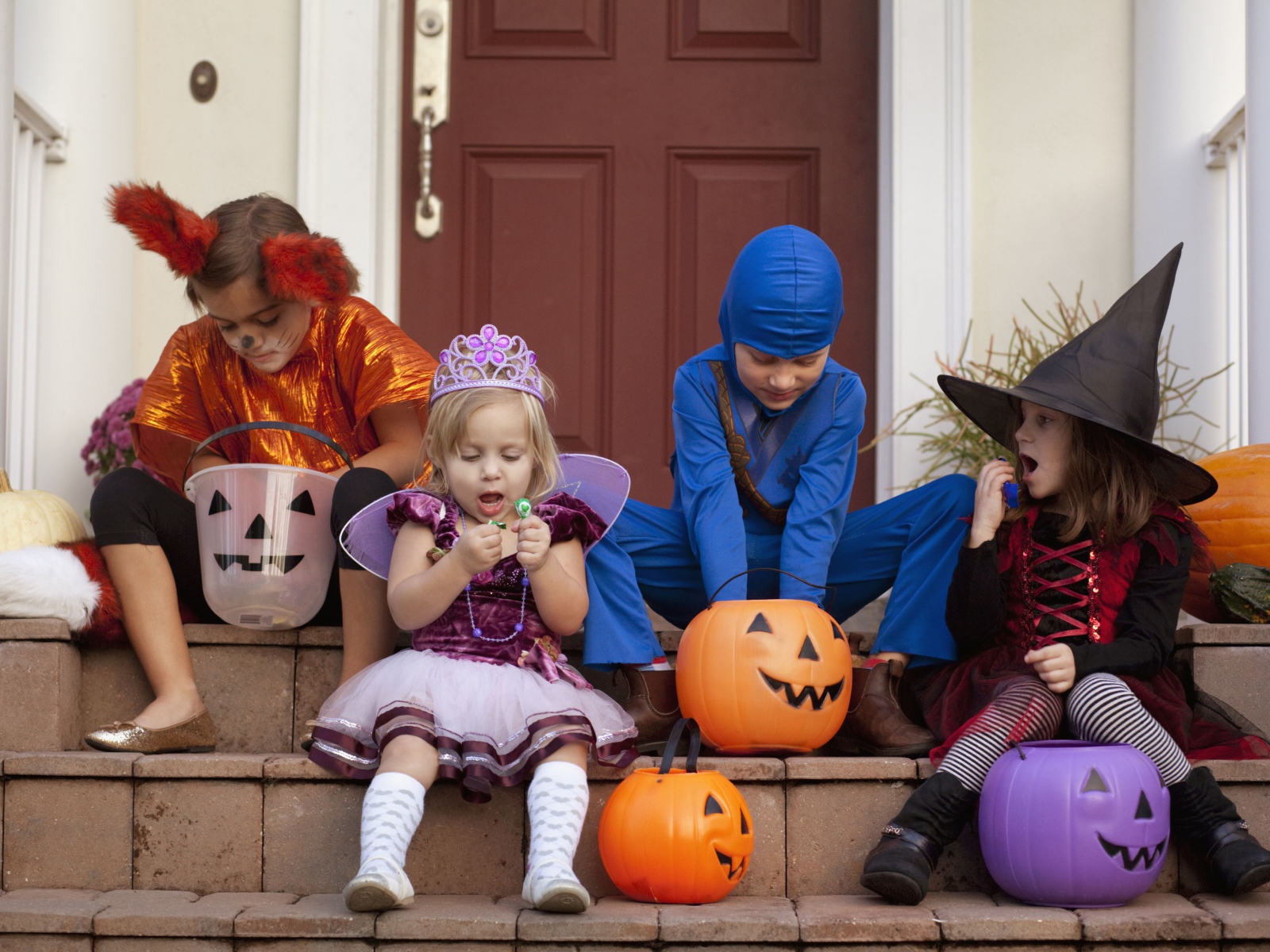 Маленькие дети в костюмах на Хэллоуин сидят на ступеньках со сладостями
