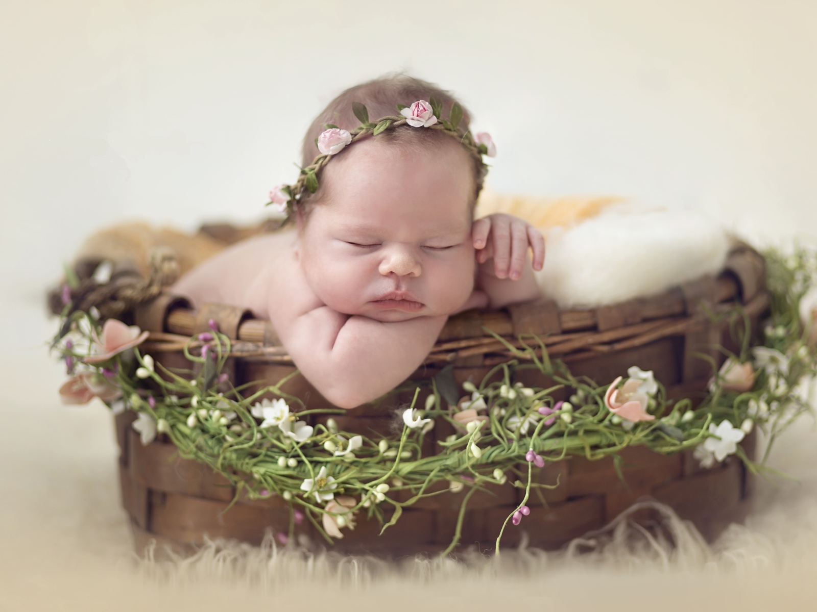 Спящий грудной ребенок в корзине с венком из цветов