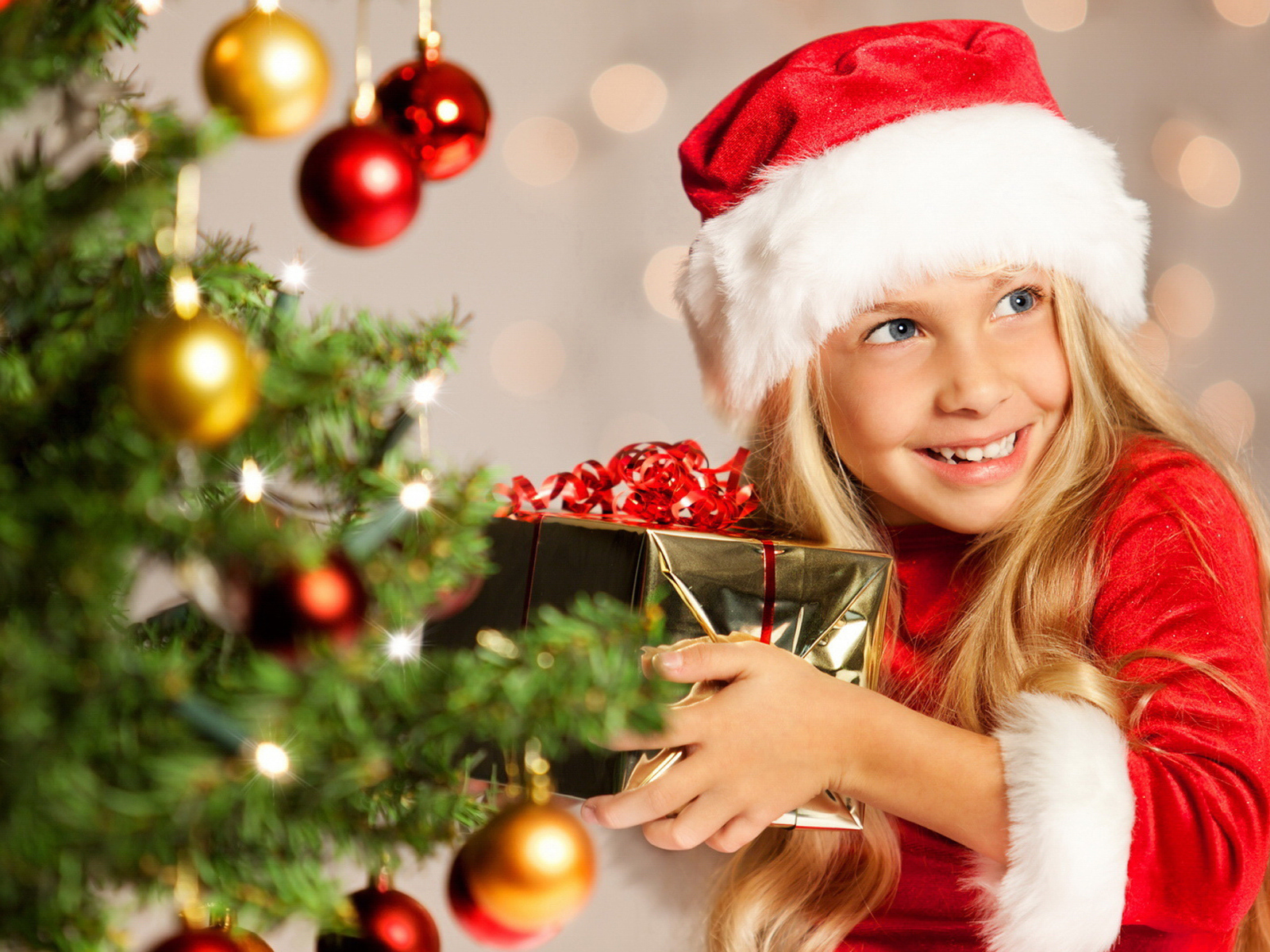 Улыбающаяся девочка блондинка с подарком у елки на новый год 