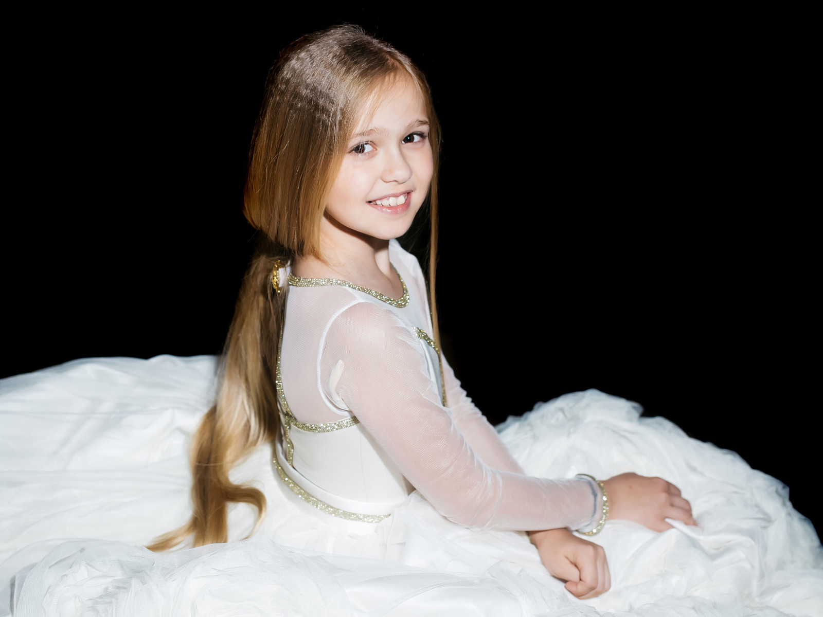 Улыбающаяся девочка в красивом белом платье на черном фоне