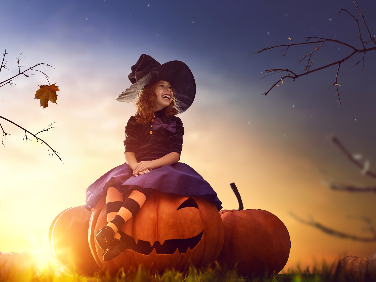 Улыбающаяся девочка сидит на тыкве в костюме на Хэллоуин 