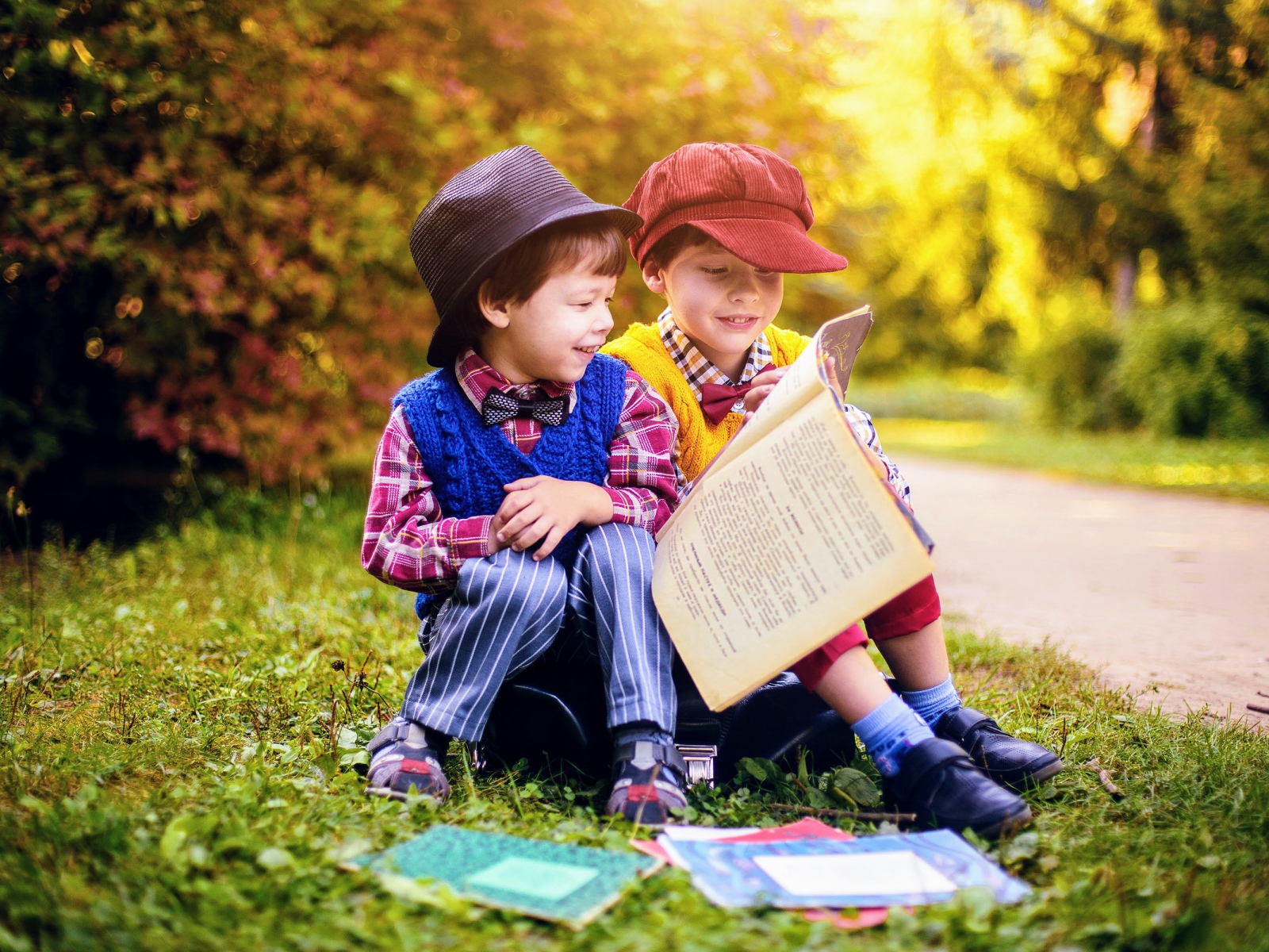 Two little boys read a book while sitting on the grass