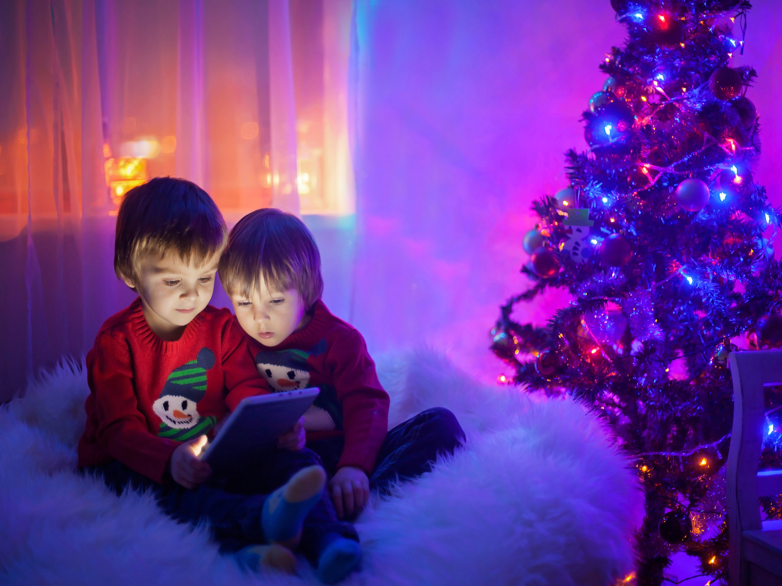 Two little boys watching cartoons by the New Year tree