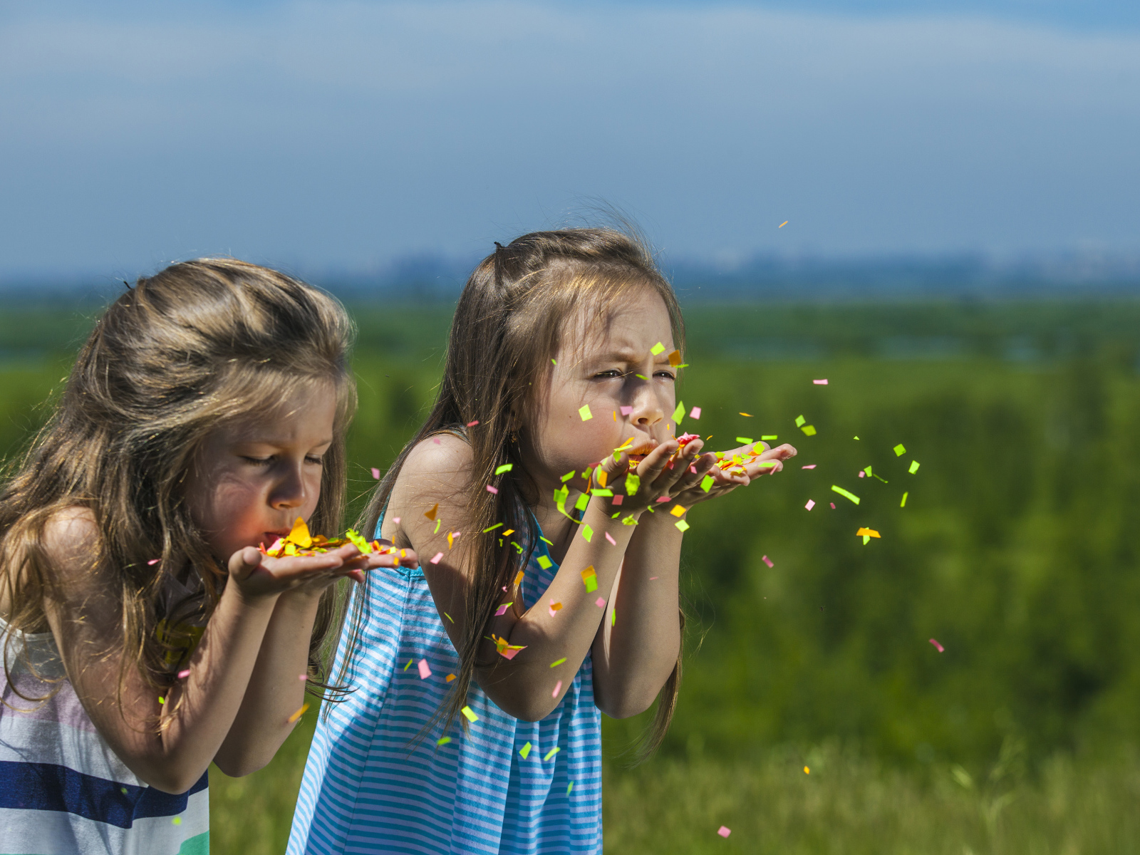 Две маленькие девочки сдувают конфетти  с рук