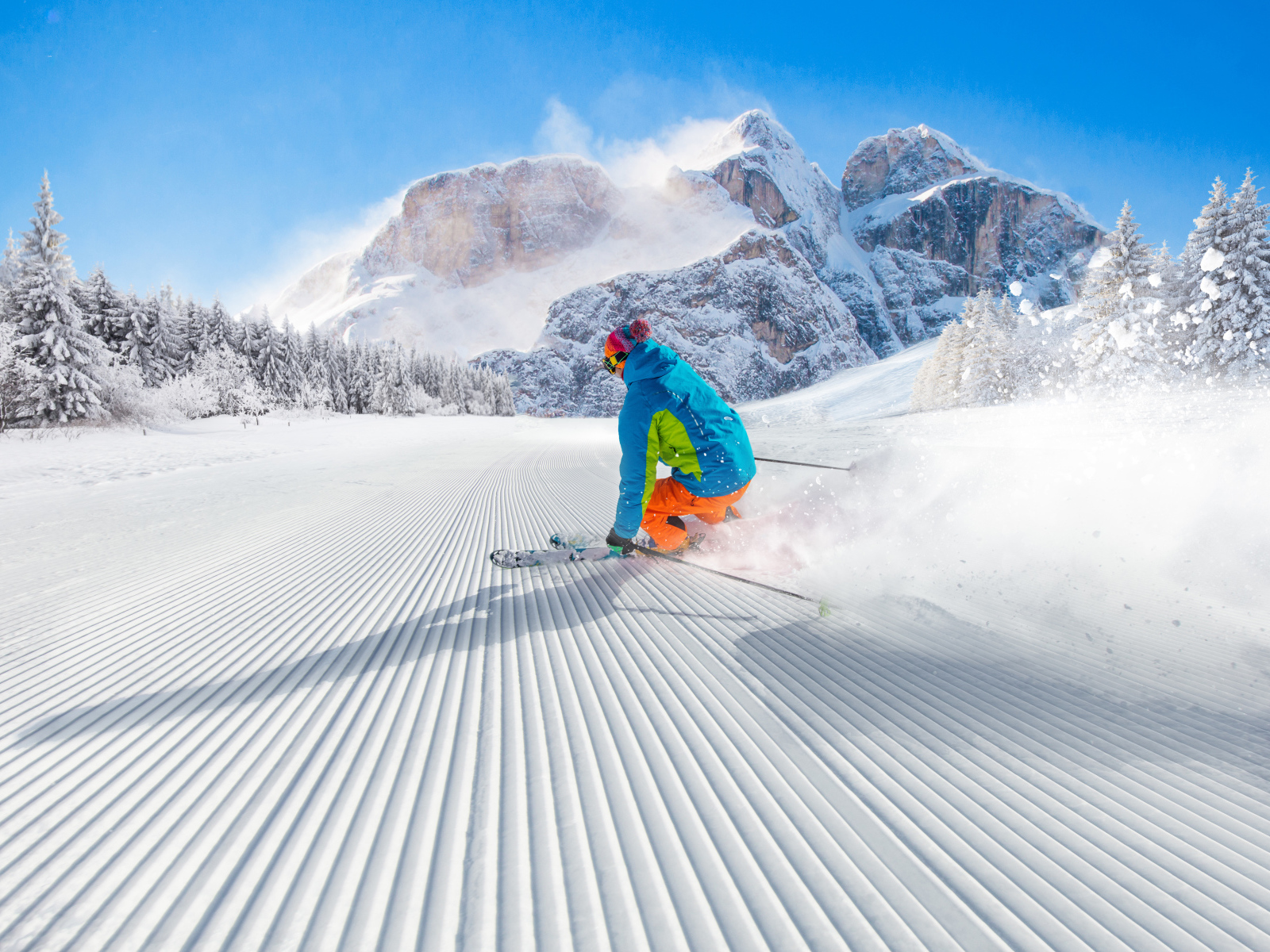 Лыжник спускается по склону на фоне заснеженных гор 