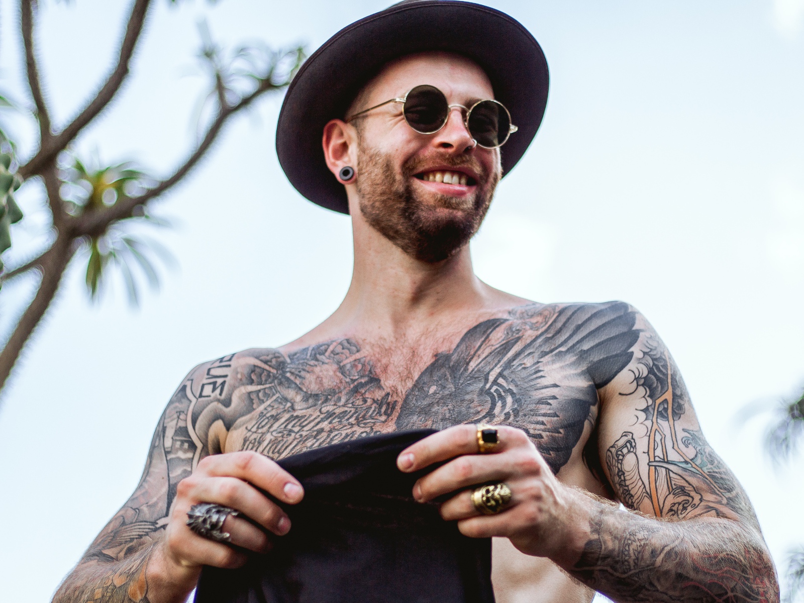 Мужчина с татуировками на теле в черной шляпе и очках