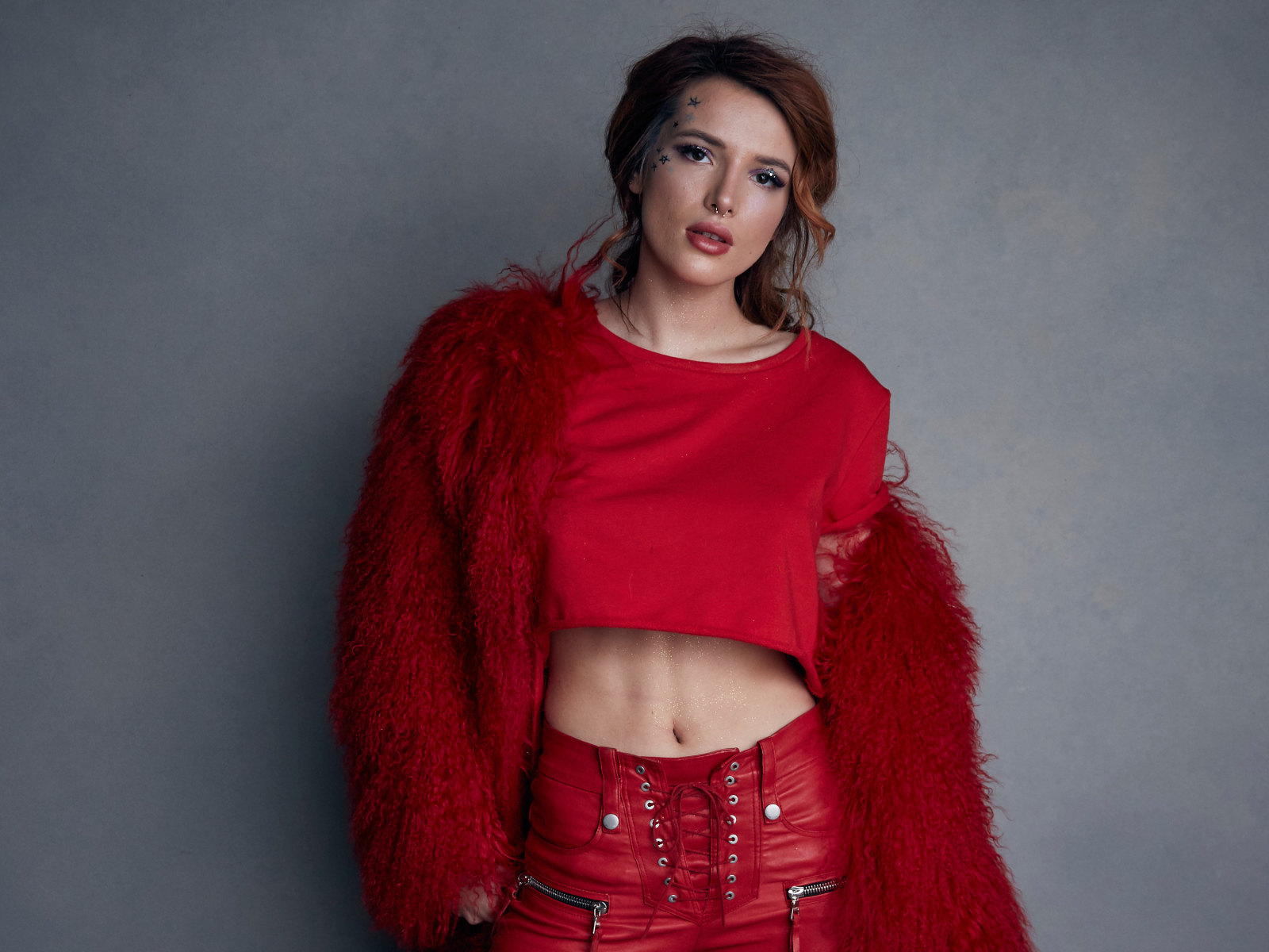 Актриса Белла Торн в красном наряде на фоне серой стены 