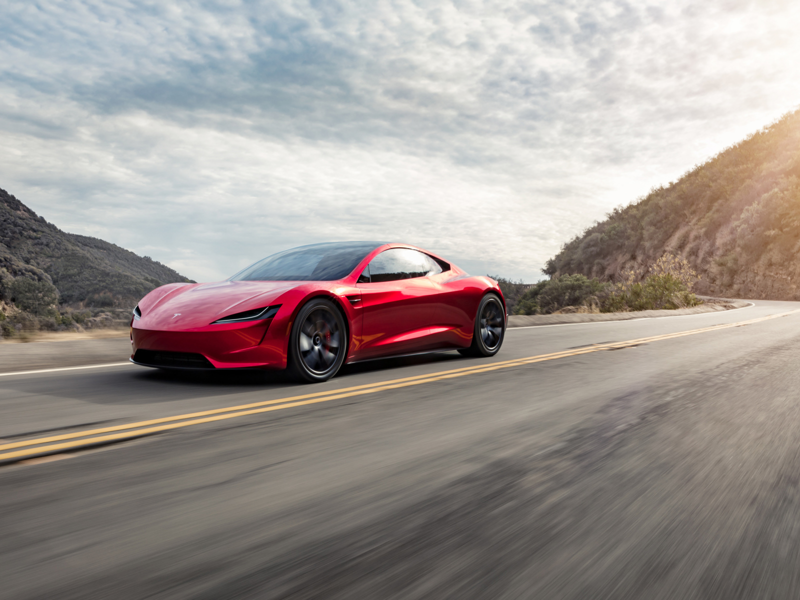 Красный автомобиль Tesla Roadster едет по трассе 