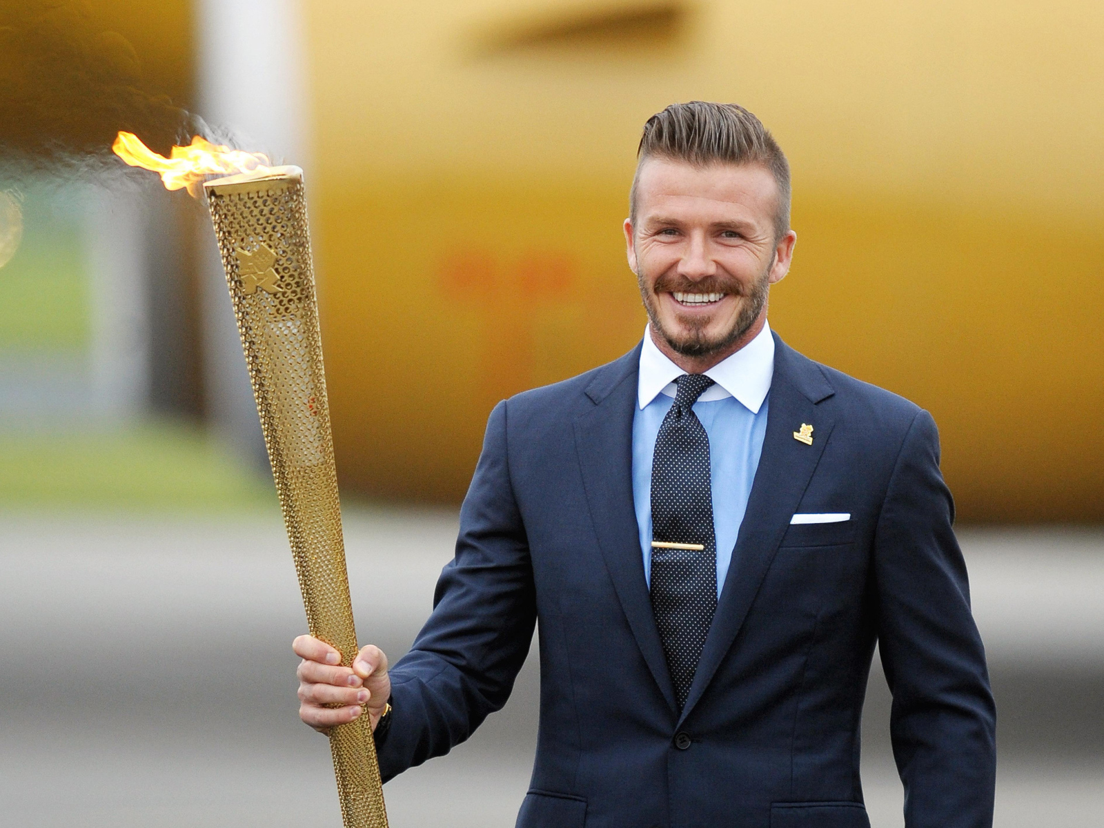 Улыбающийся футболист Дэвид Бекхэм с олимпийский огнем в руке