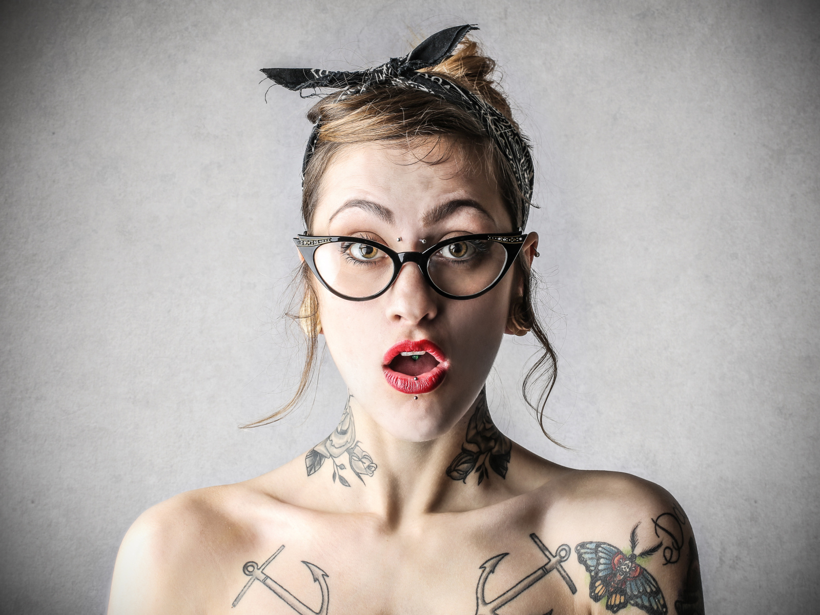 Удивленная девушка в очках с татуировками на теле
