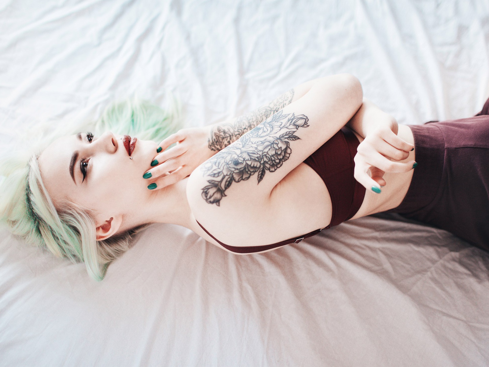Девушка с татуировкой на руке лежит на кровати 