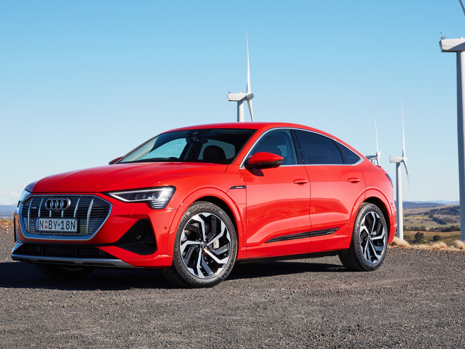 Красный автомобиль Audi E-Tron 50 Quattro Sportback S Line 2020 на фоне ветряных турбин