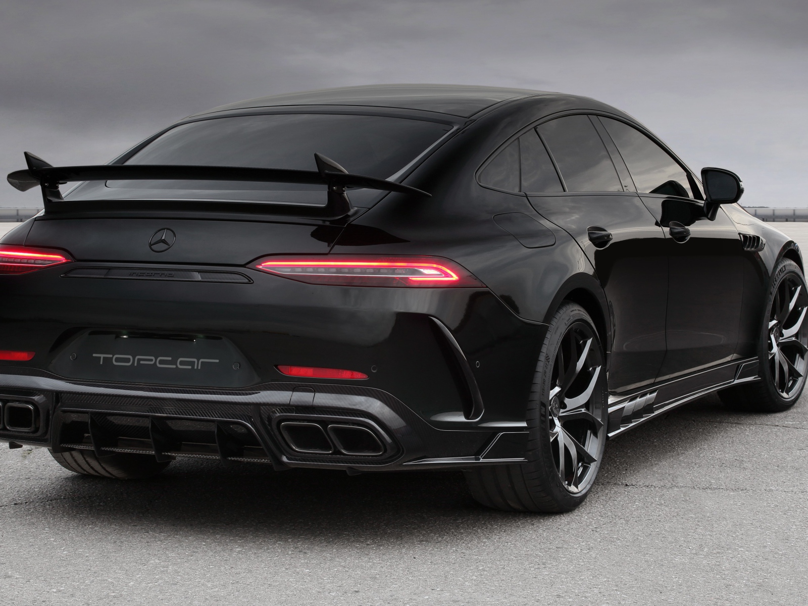 Черный автомобиль Mercedes-AMG GT 63 S 4MATIC+, 2020 года вид сзади на сером фоне