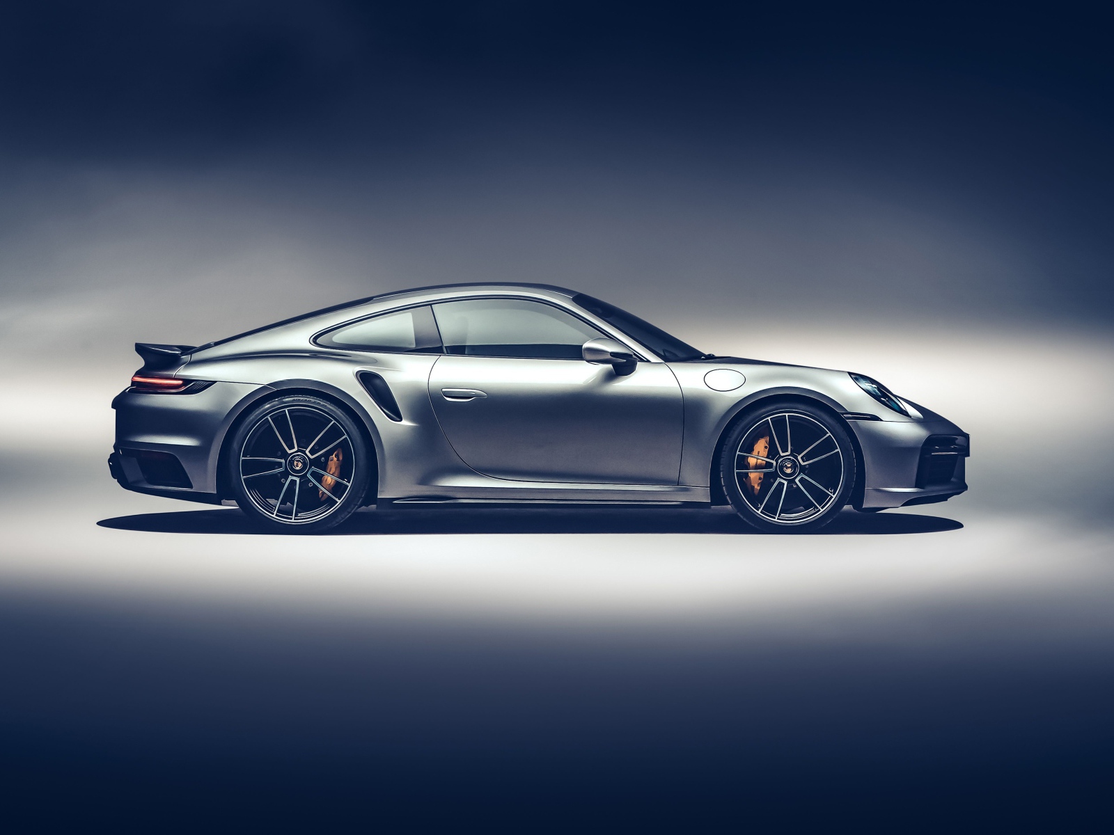 Серебристый автомобиль Porsche 911 Turbo S 2020 года вид сбоку на сером фоне