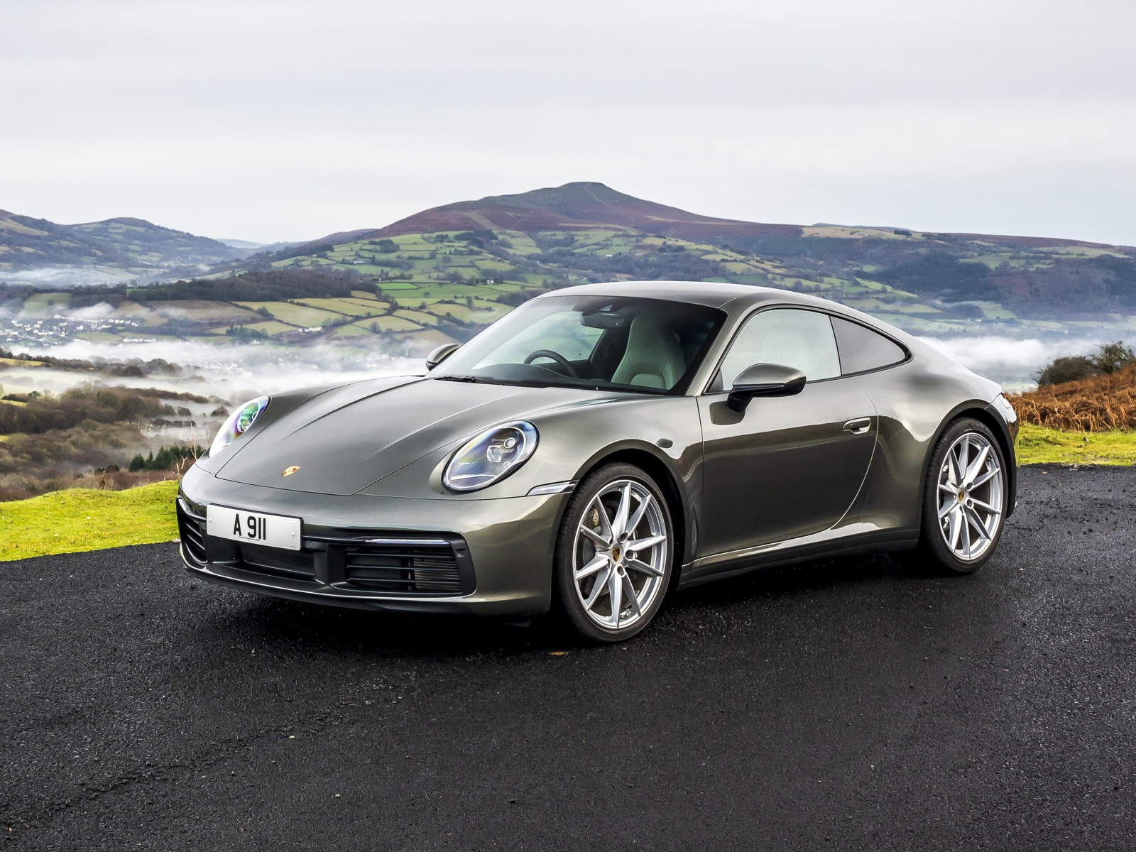 Серебристый автомобиль Porsche 911 Carrera на фоне холмов