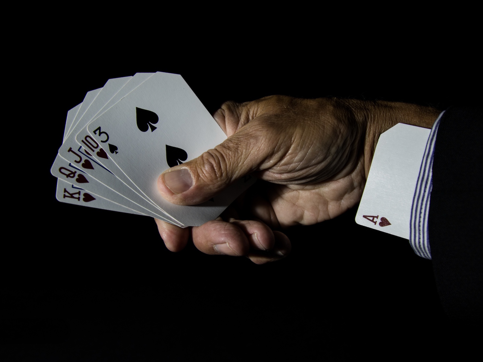 Туз в рукаве у шулера на черном фоне 