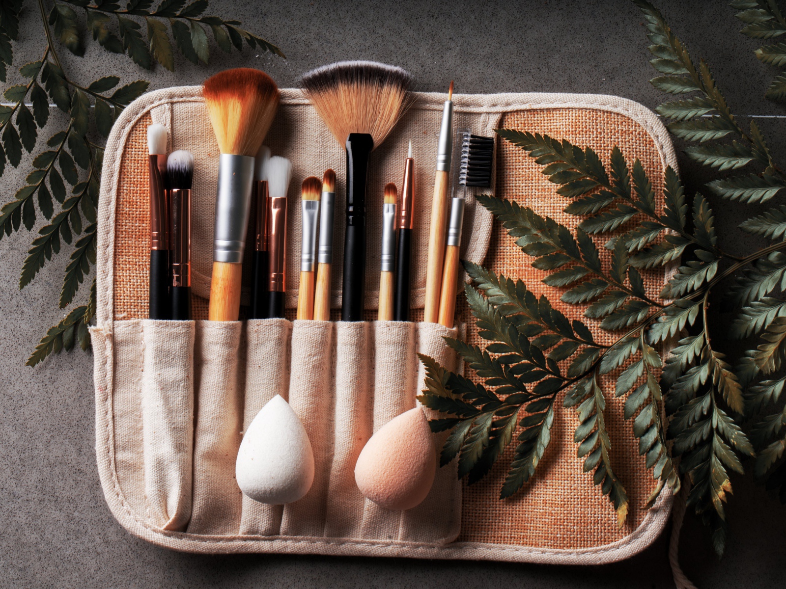 Кисти для макияжа в чехле на столе с листьями папоротника