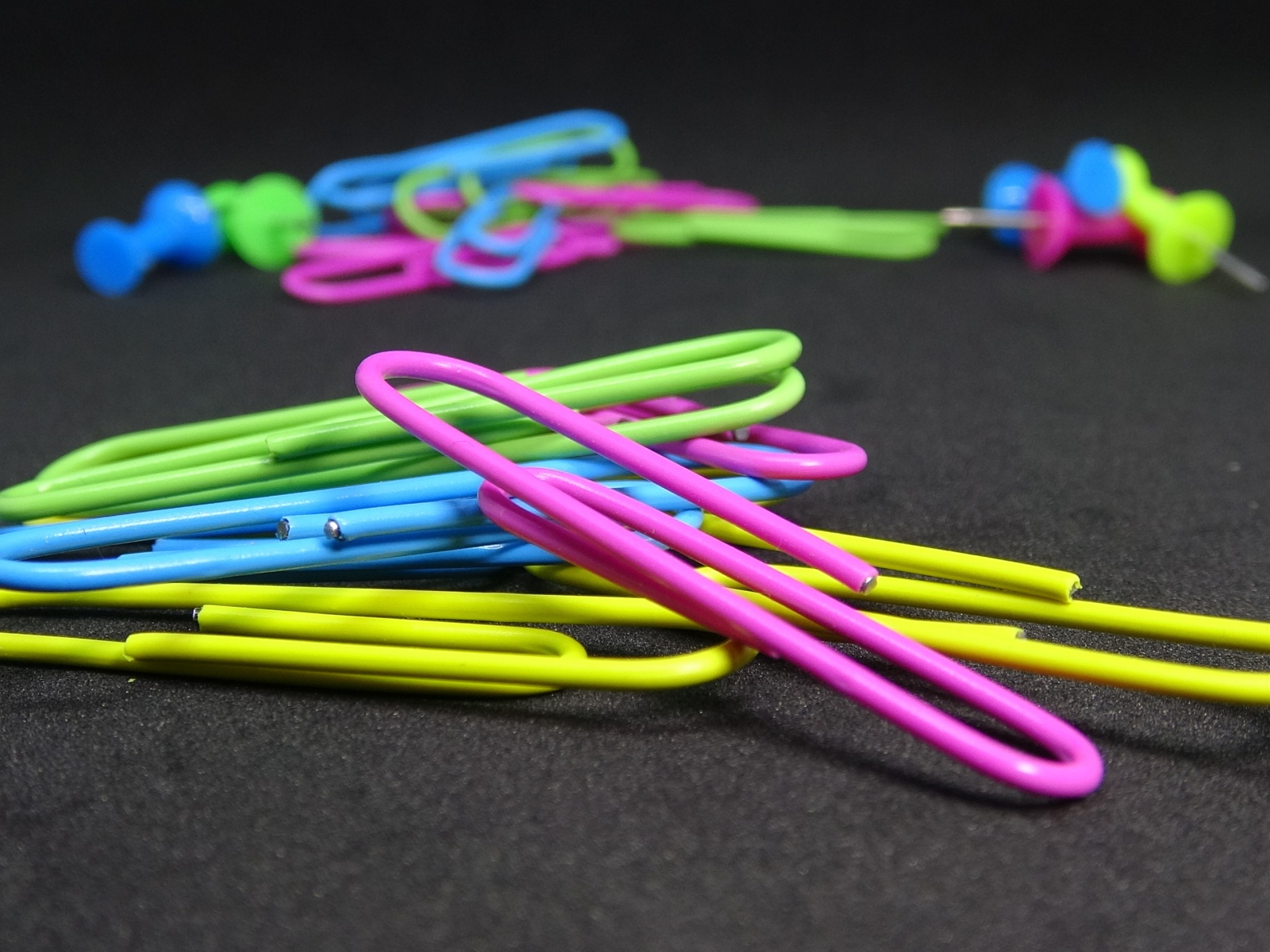 Разноцветные скрепки на черном столе 
