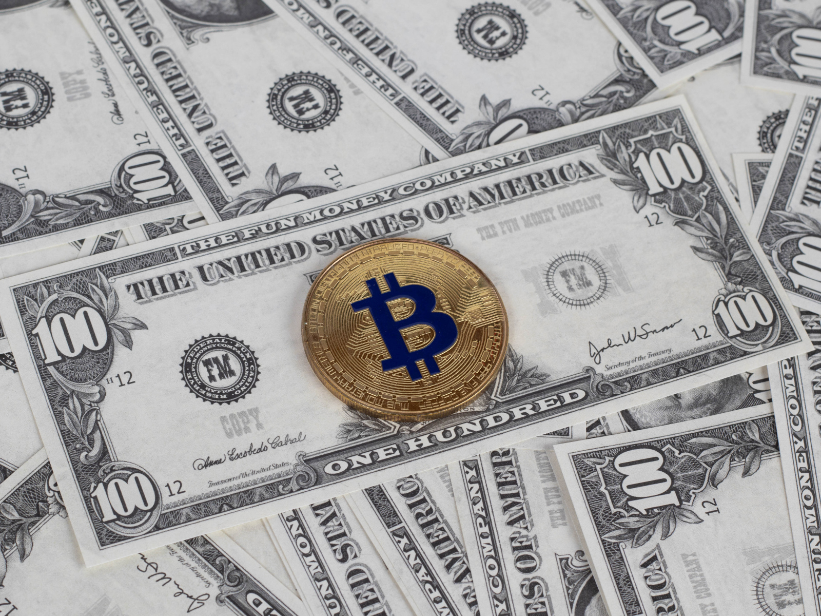 Монета Биткоин лежит на стодолларовых купюрах