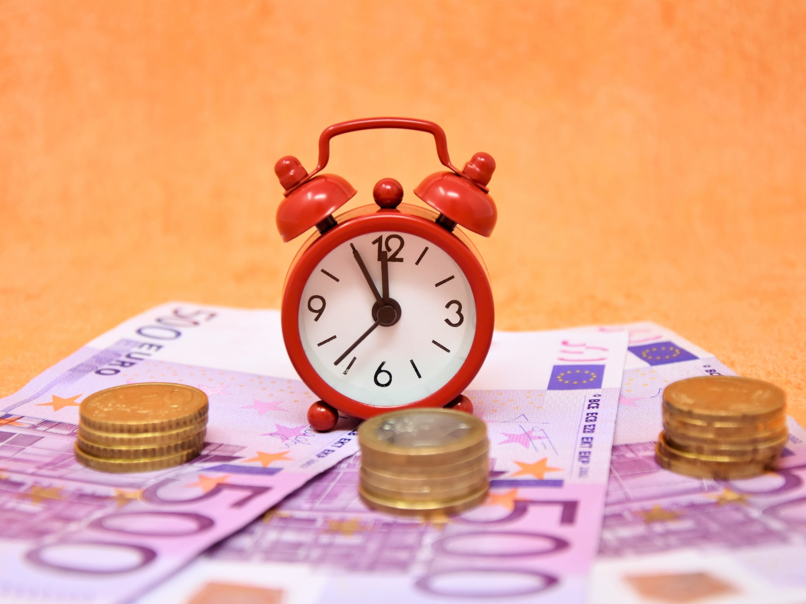 Маленький красный будильник с купюрами евро и монетами