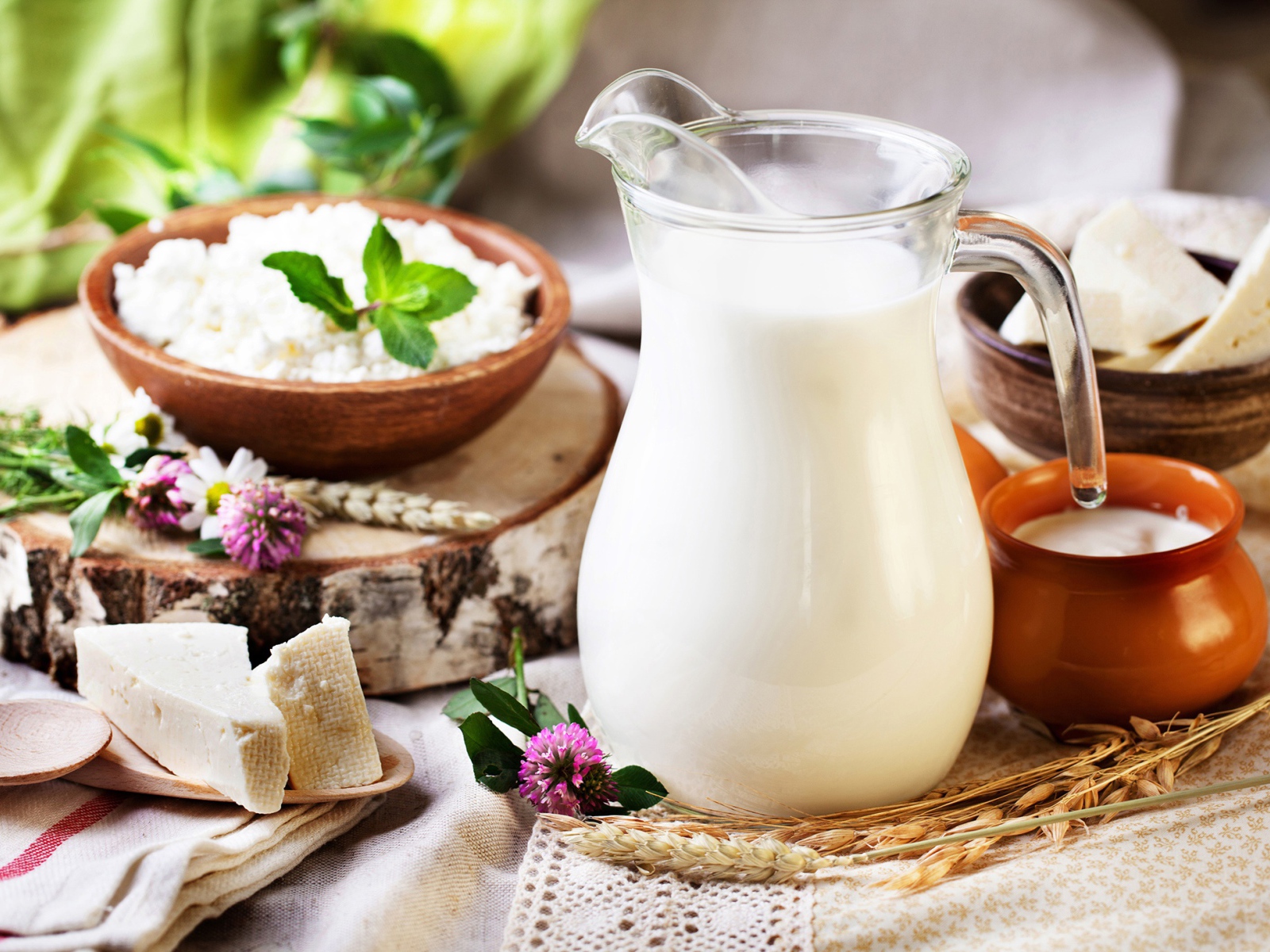 Кувшин с молоком стоит на столе с сыром и творогом