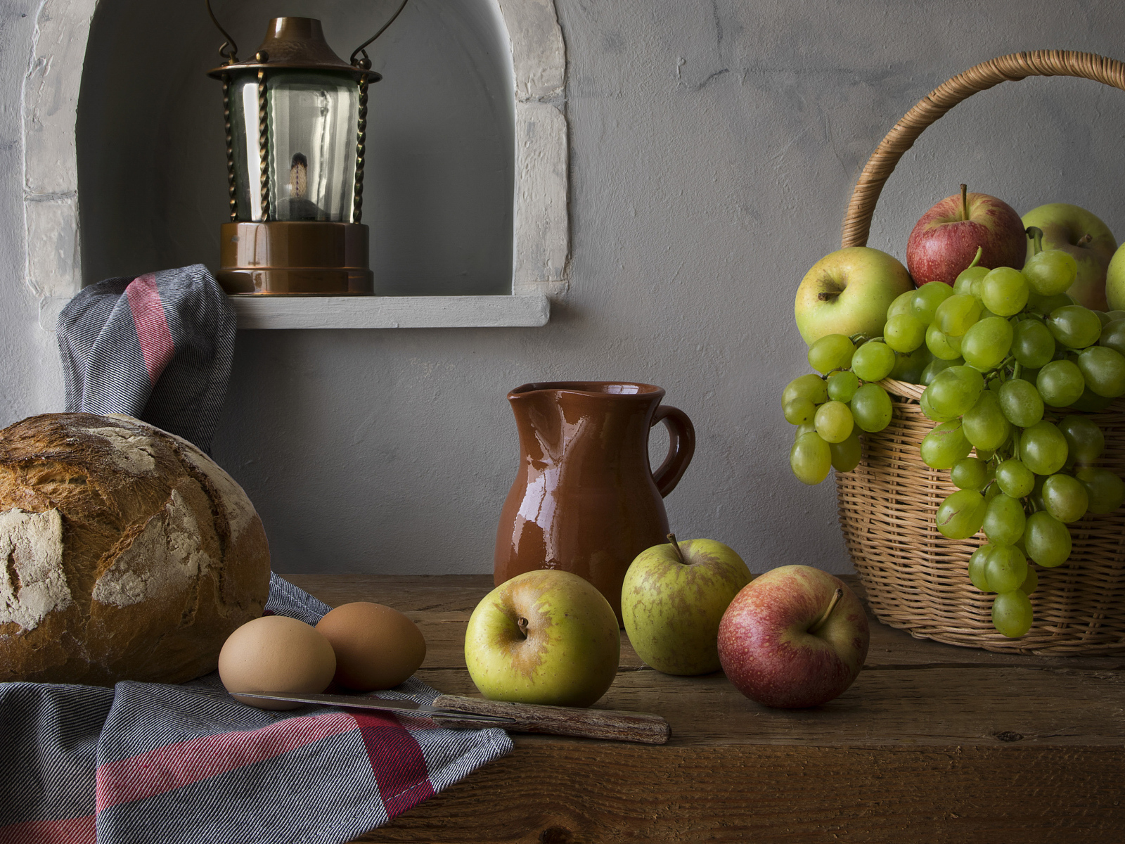 Корзина с яблоками и виноградом на столе с хлебом и яйцами
