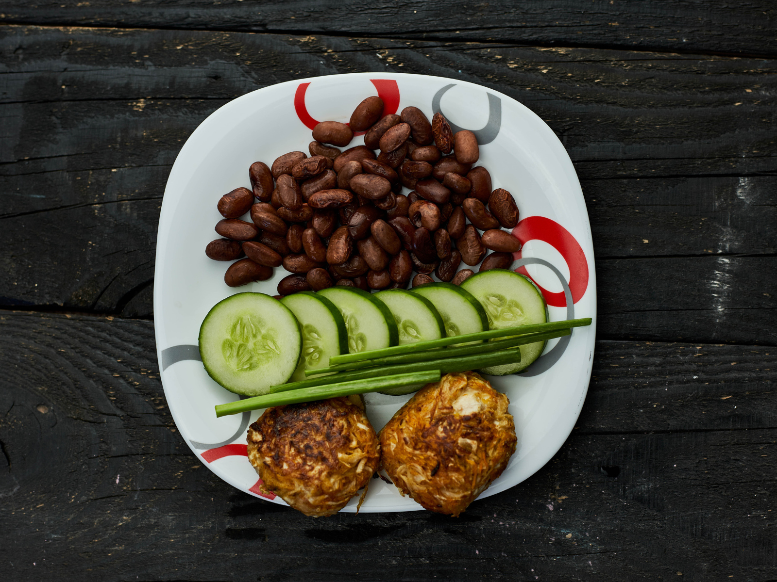 Фасоль на тарелке с оладьями и огурцами 