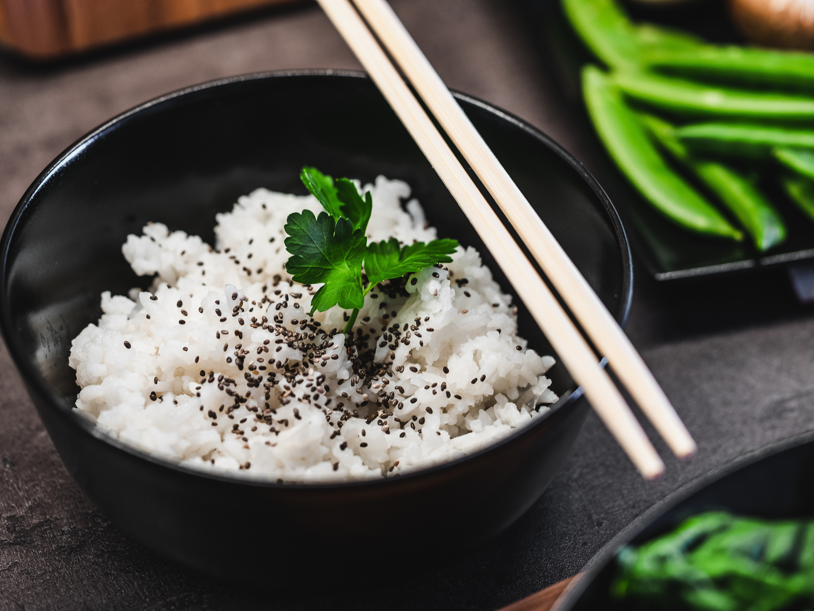 Вареный рис с семенами  в черной миске с палочками