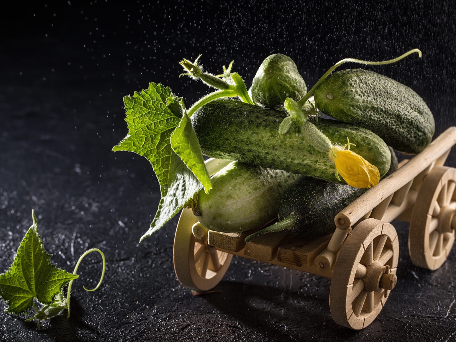 Огурцы на игрушечной тележке на черном столе