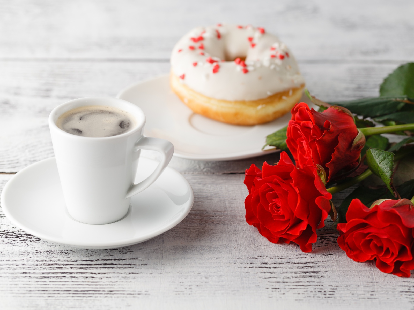 Cup of coffee, a donut and three red roses on the table
