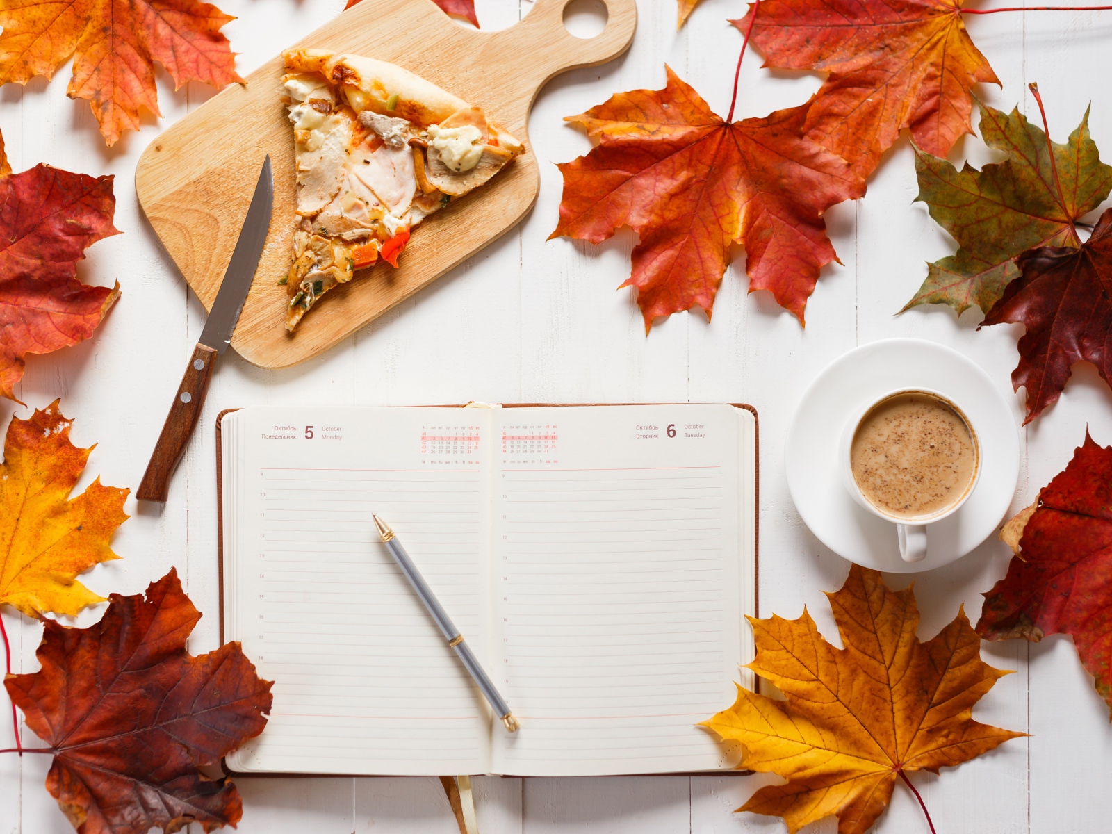 Ежедневник на столе с желтыми листьями, кофе и пиццей 