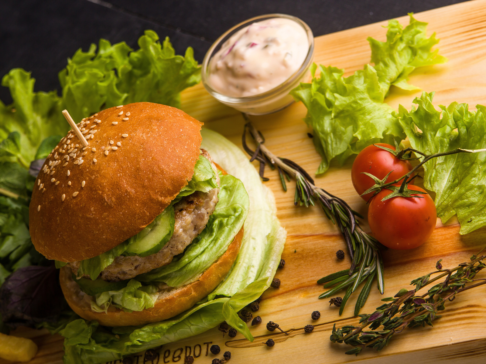 Гамбургер на столе с листьями салата, специями, помидорами и соусом