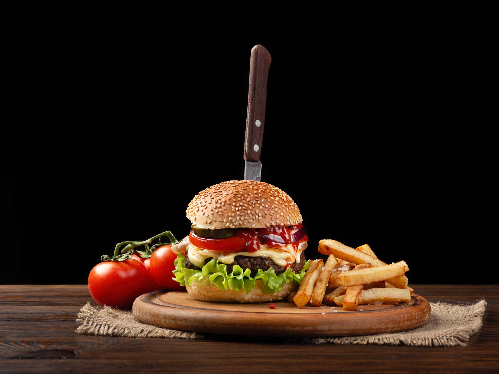 Гамбургер с ножом на столе с помидорами и картофелем фри 