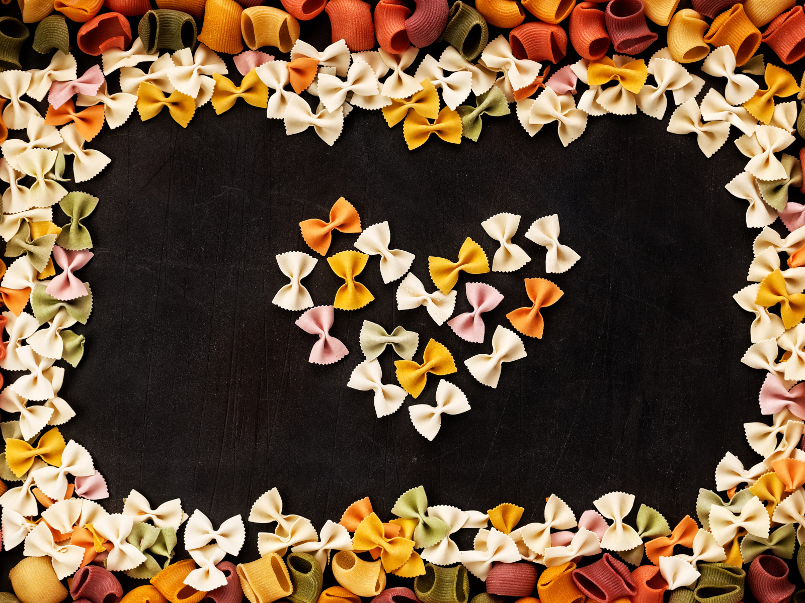 Сердце из разноцветных макарон на черном столе 