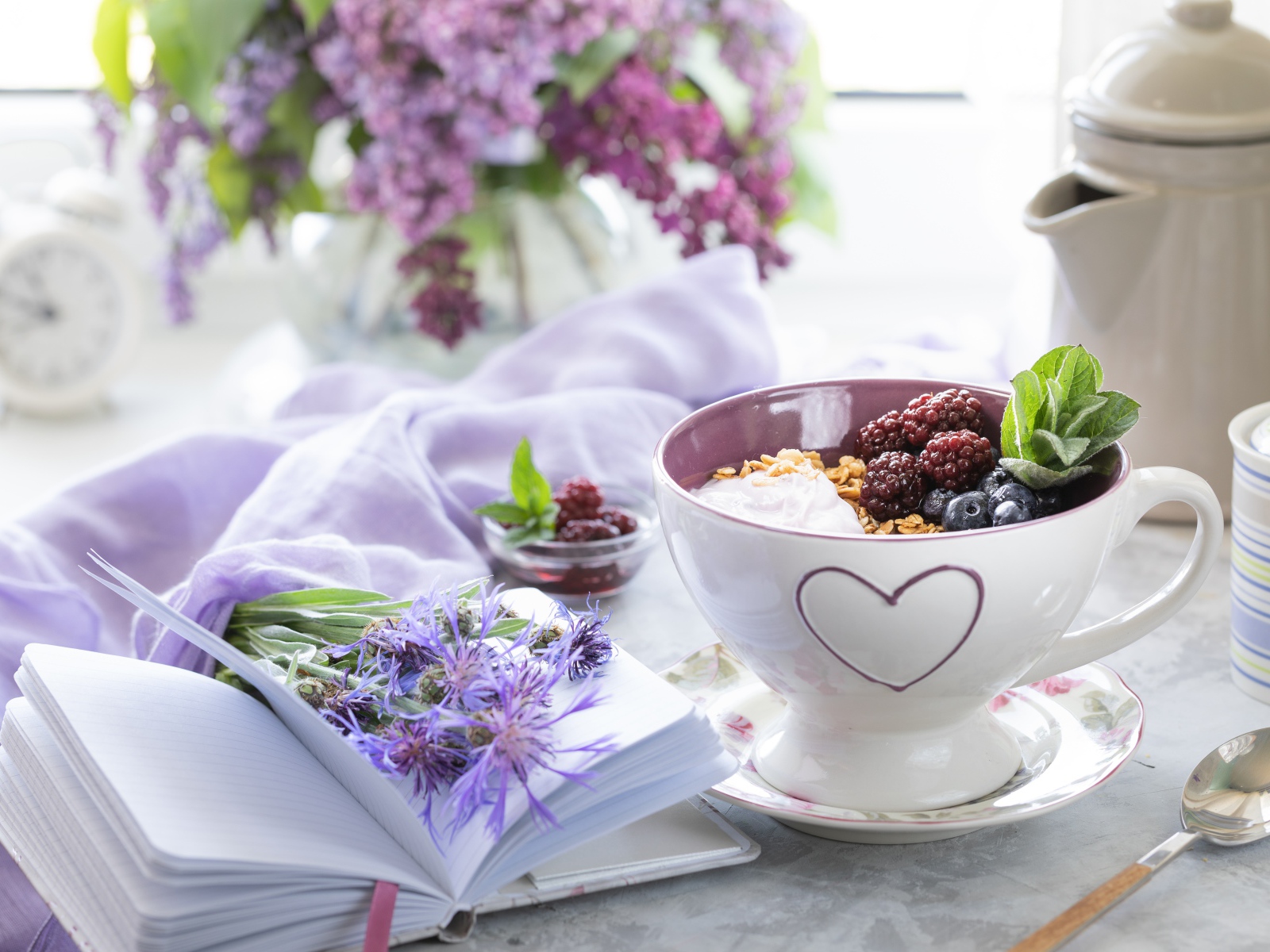 Мюсли с ягодами в чашке на столе с блокнотом и букетом сирени 