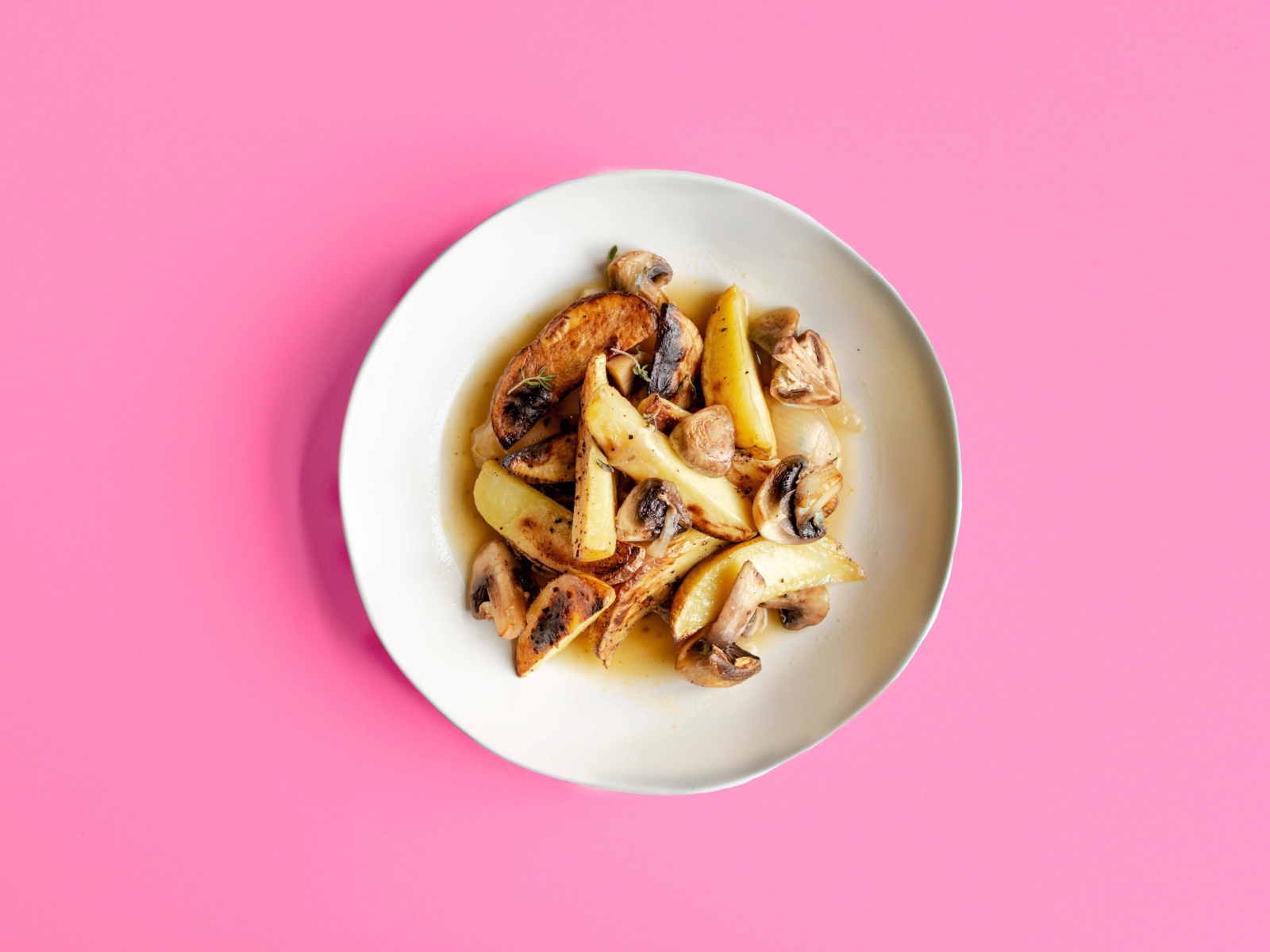 Картофель с грибами в тарелке на розовом фоне 