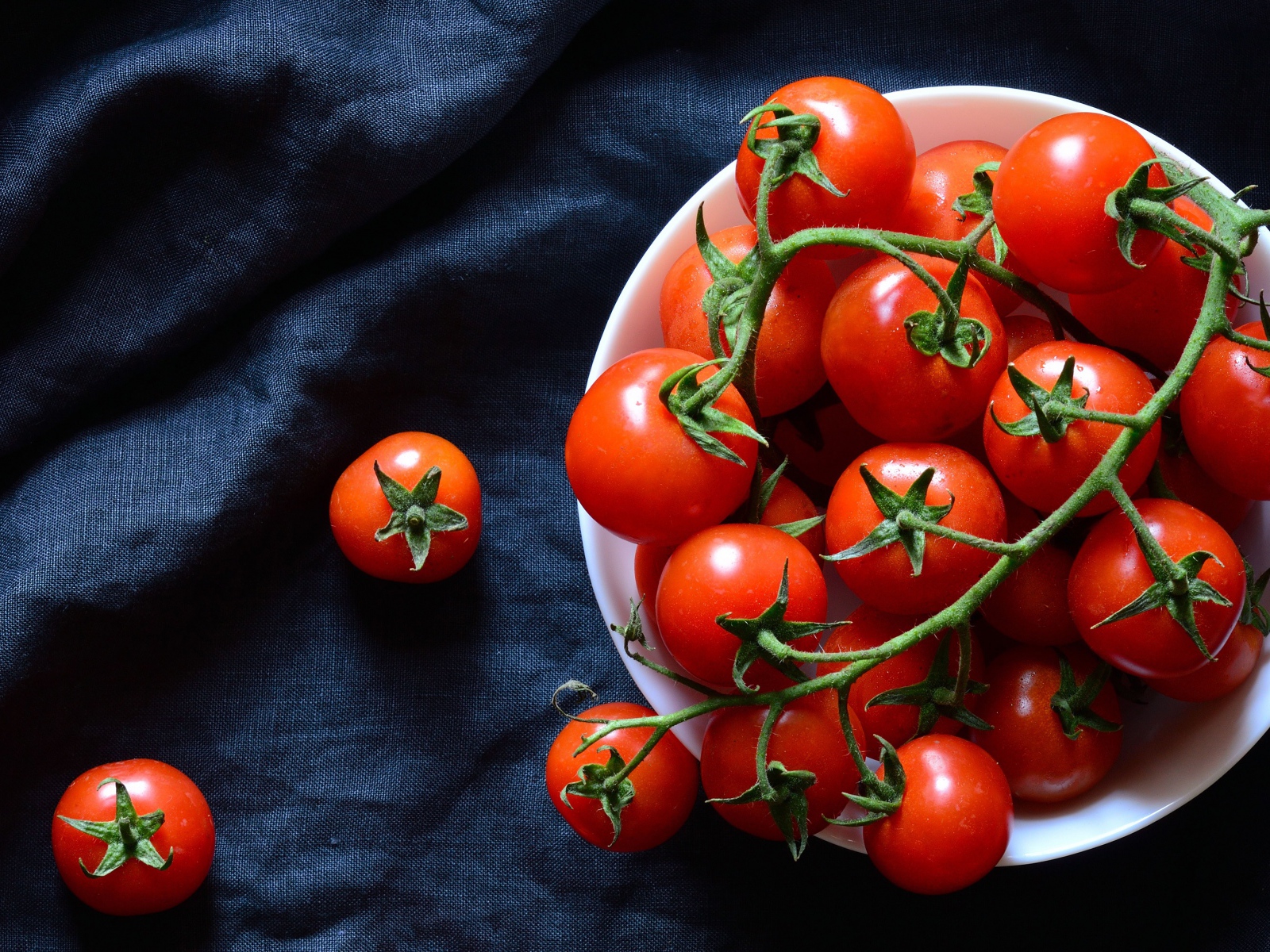 Красные помидоры в белой миске на черном фоне