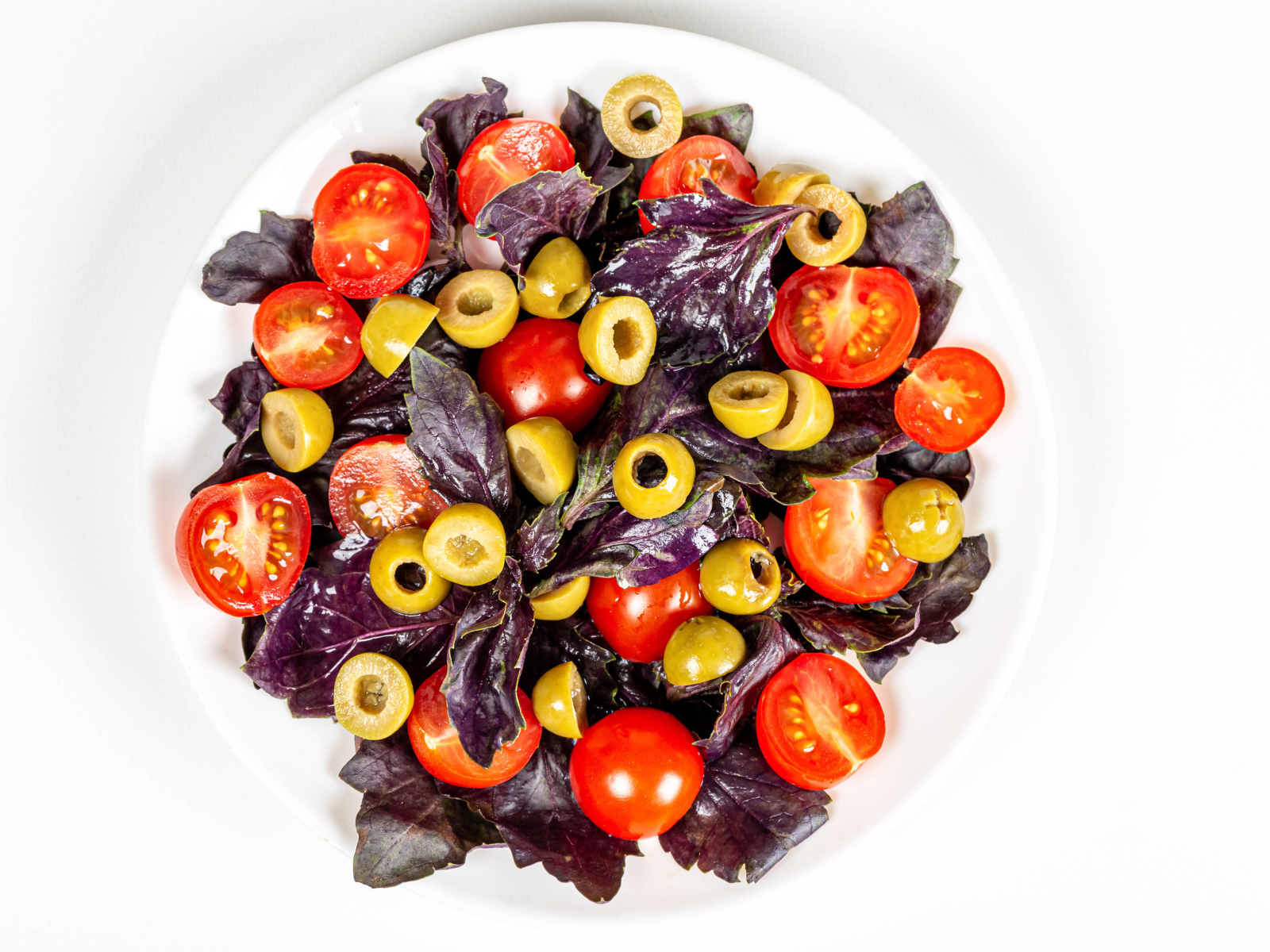 Салат с листьями базилика, помидорами и оливками на белом фоне