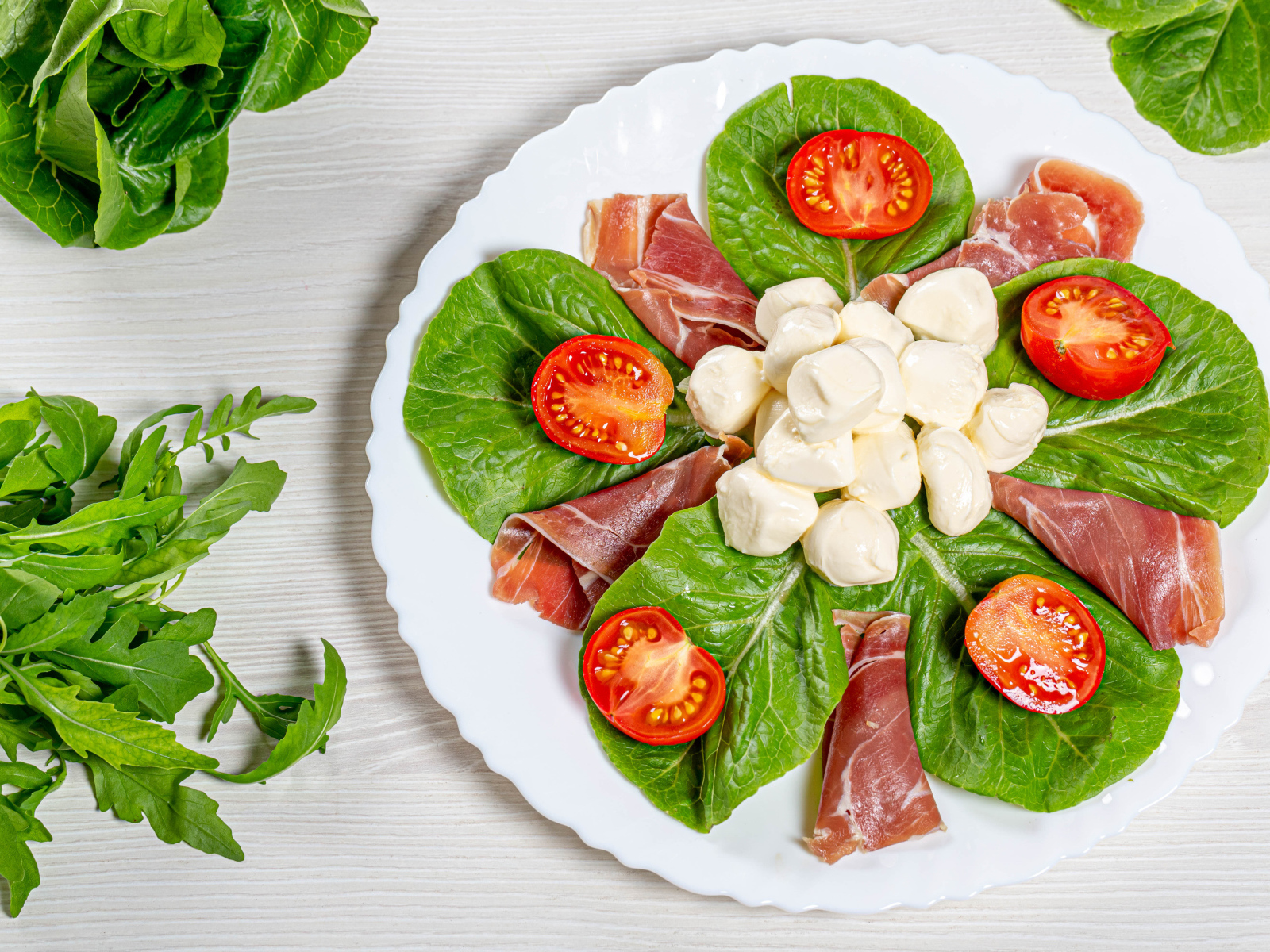 Кусочки ветчины на тарелке с сыром, помидорами и листьями салата