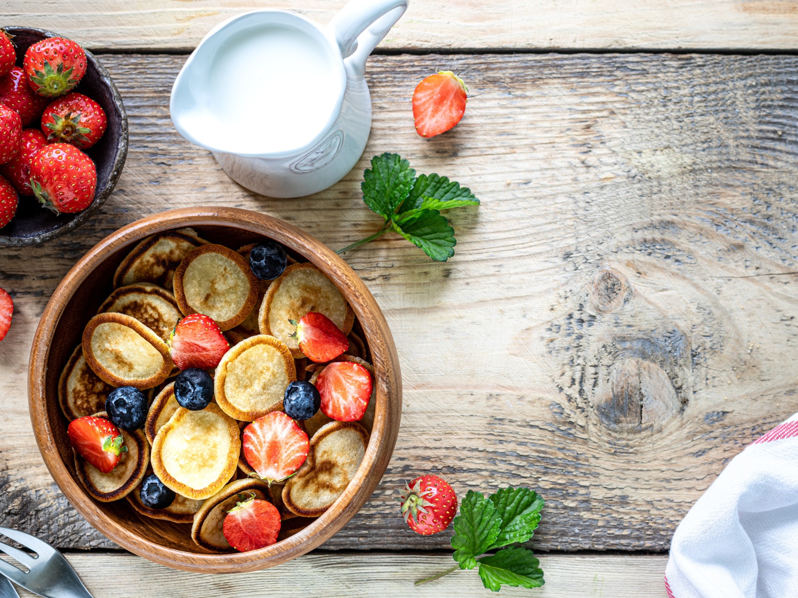 Маленькие оладьи в миске с клубникой и черникой на столе с молоком 