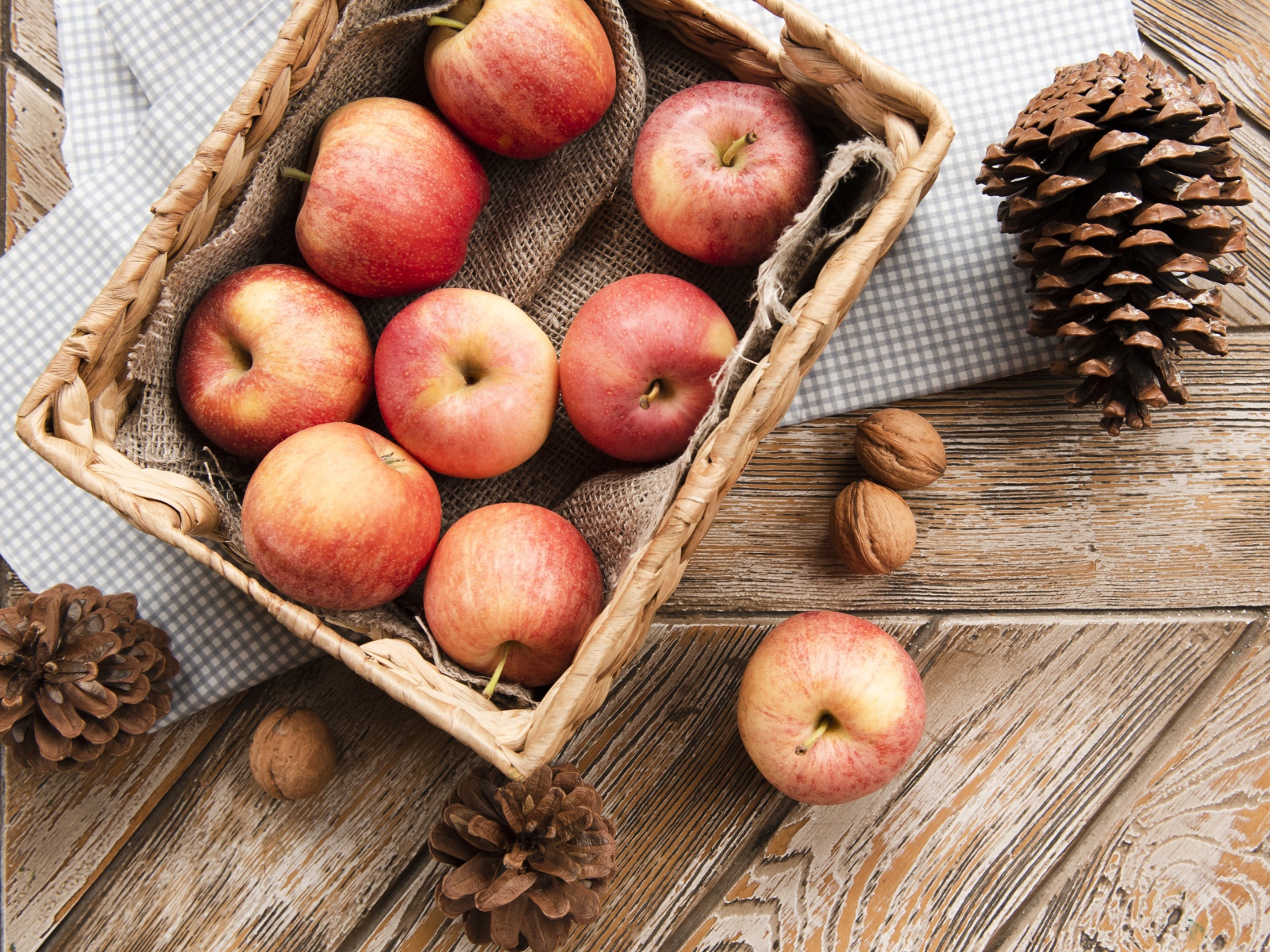 Корзина с яблоками на столе с сосновыми шишками