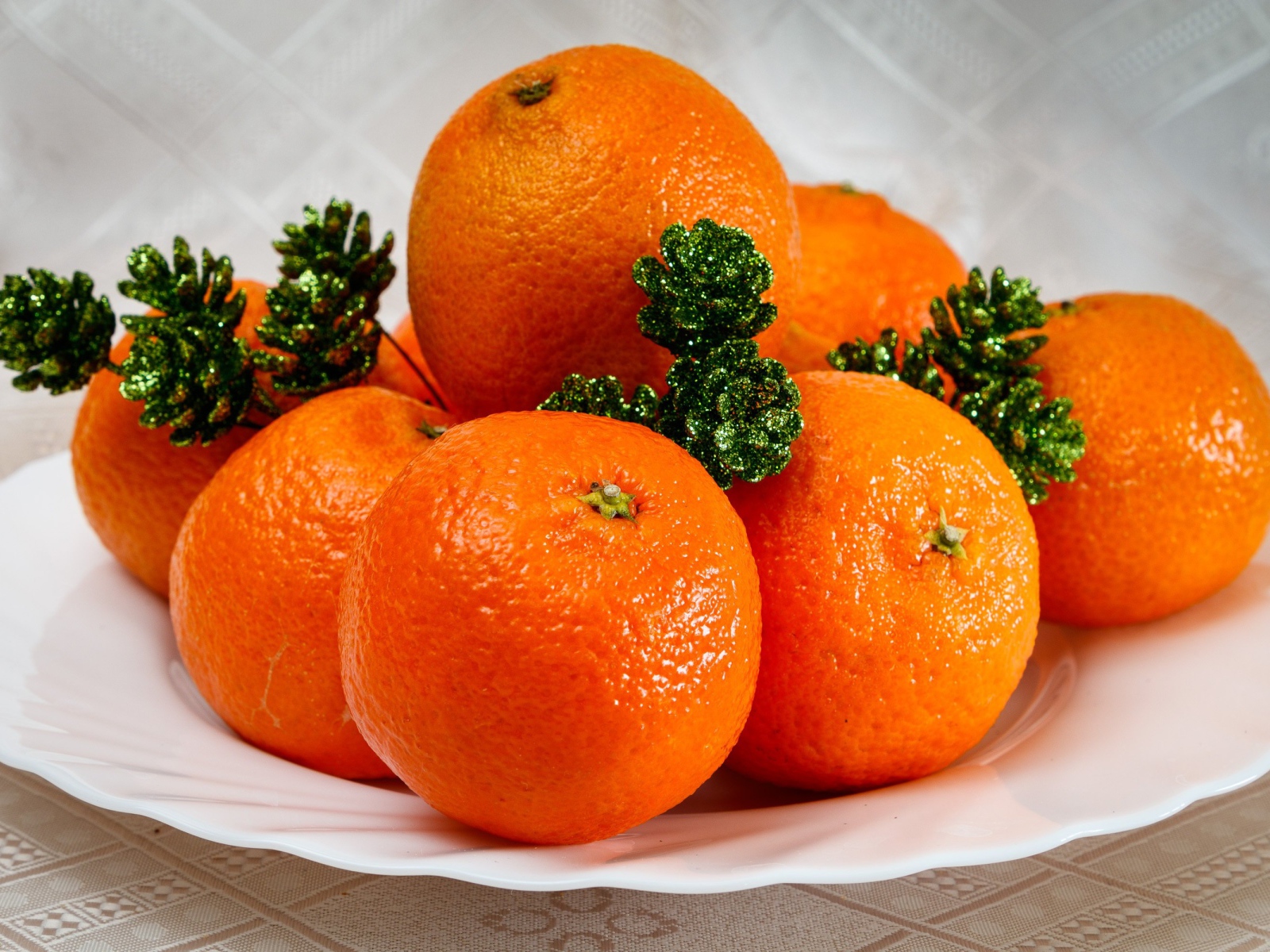 Много оранжевых мандаринов на тарелке с шишками