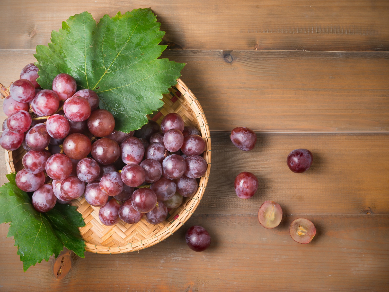 Розовый виноград с зелеными листьями на деревянном столе 